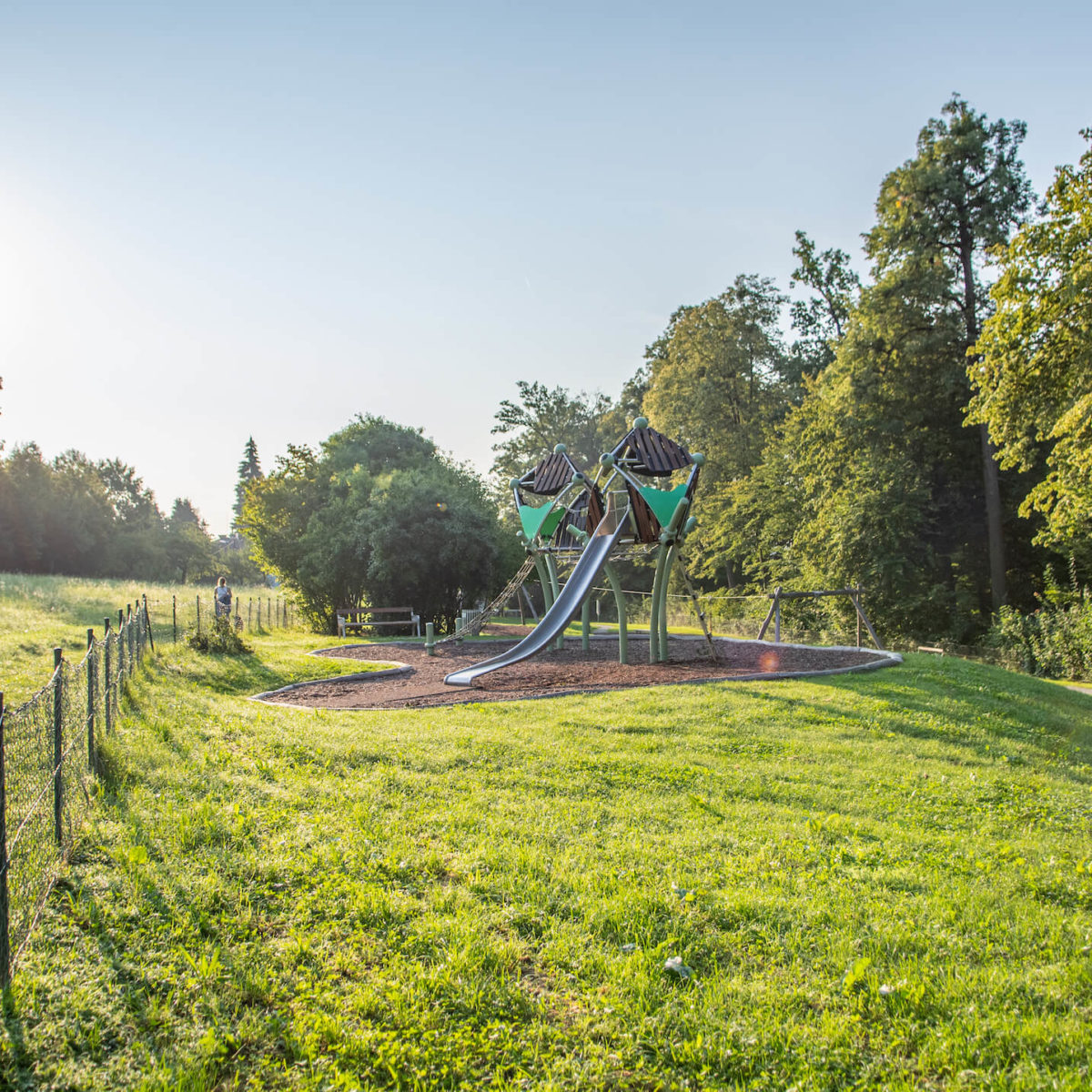 A playground with a slide in a grassy area surrounded by trees.