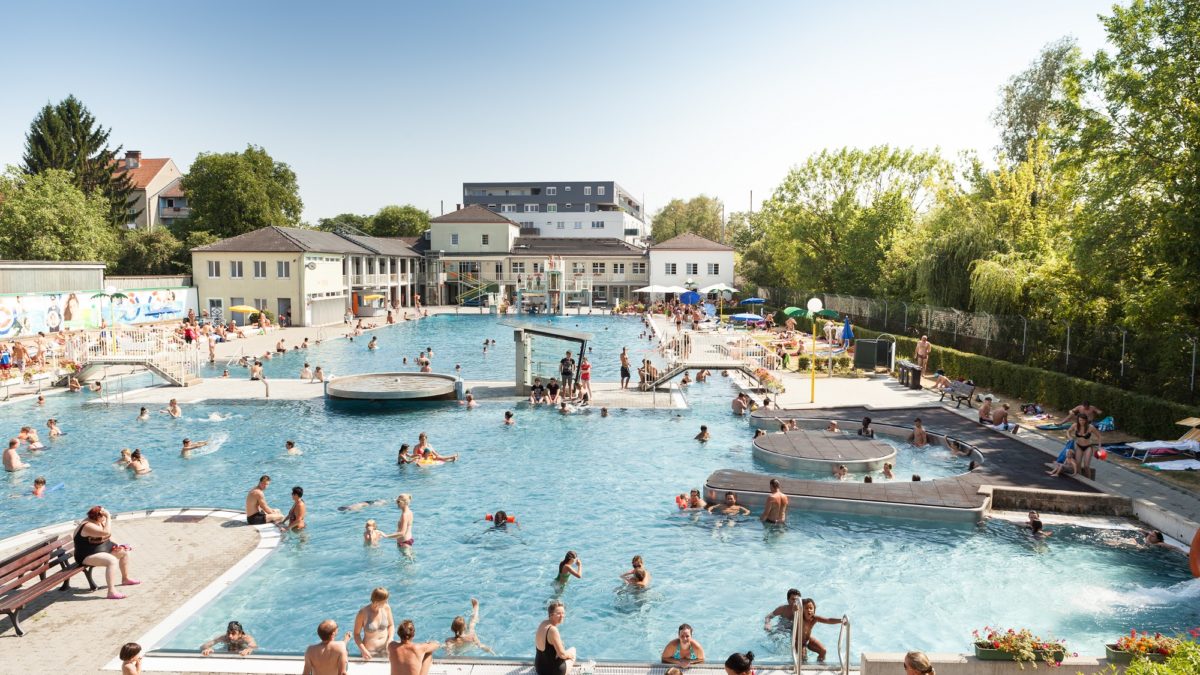 Aerial view of the Augarten swimming pool in Vienna, Austria, filled with swimmers on a sunny day.