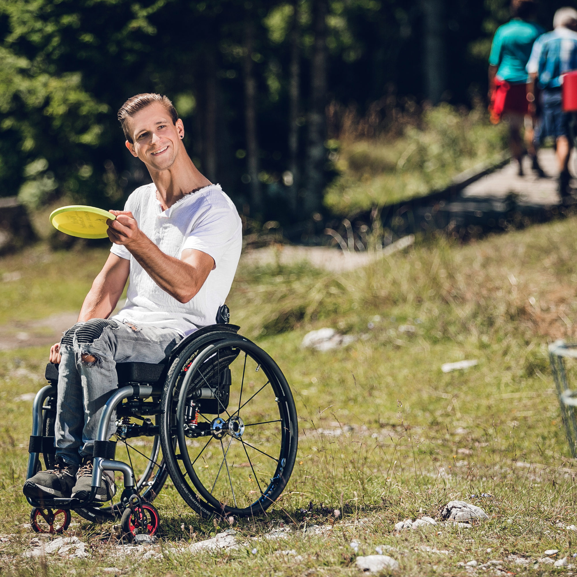 Rollstuhlfahrer spielt Disc Golf am Schöckl. Er hält Frisbee in Hand und visiert Korb an.