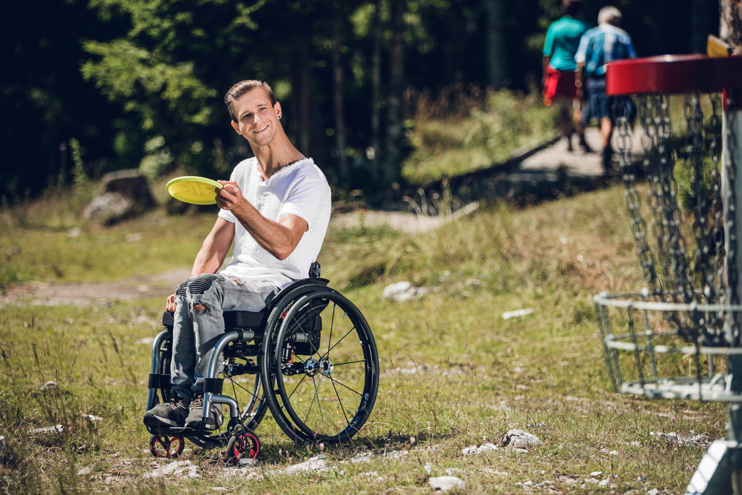 Rollstuhlfahrer spielt Disc Golf am Schöckl. Er hält Frisbee in Hand und visiert Korb an.