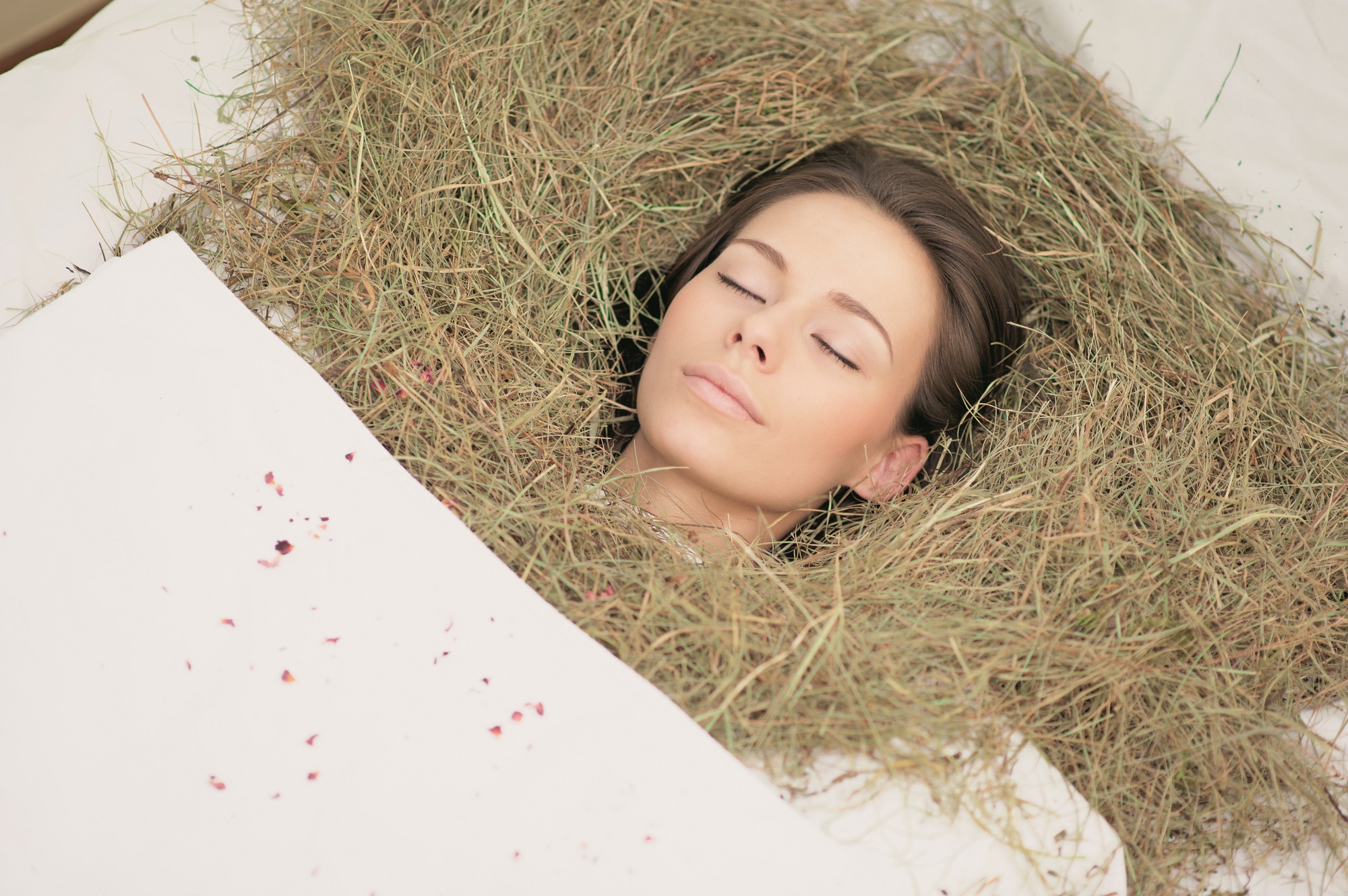 A woman lies in a hay bath at the Spa zur Sonne, eyes closed.