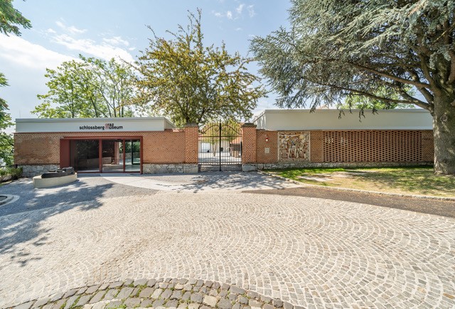 Modernes Backsteingebäude des Schlossbergmuseums mit Eingangstür, Bäumen und gepflastertem Vorplatz.