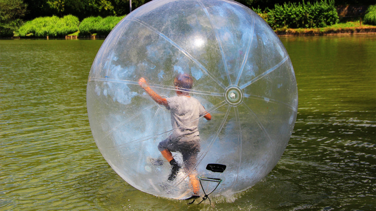 A boy runs inside a clear inflatable ball on a lake.