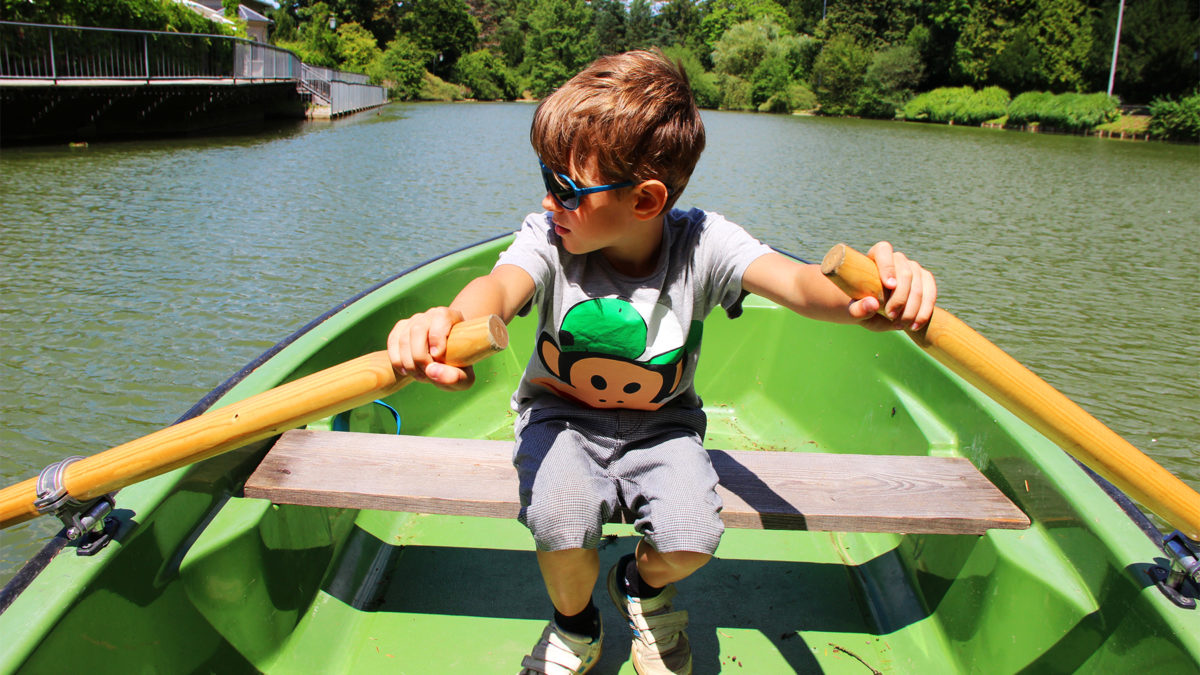 A young boy rows a green rowboat on the Hilmteich pond. He is wearing a t-shirt with a monkey on it.