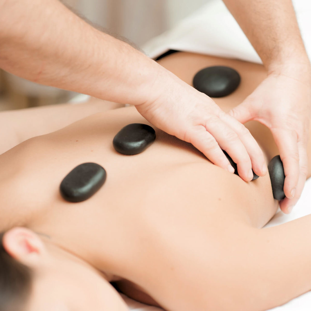A person's back is being massaged with smooth black stones.