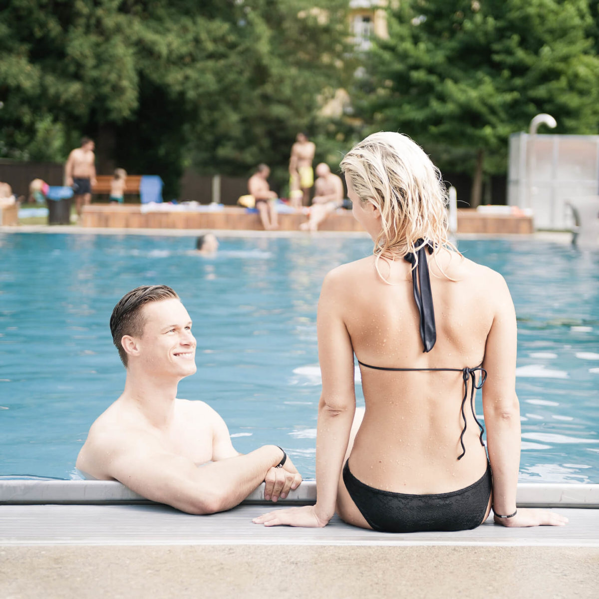 A couple sits by the edge of a pool at Margaretenbad, smiling at each other.