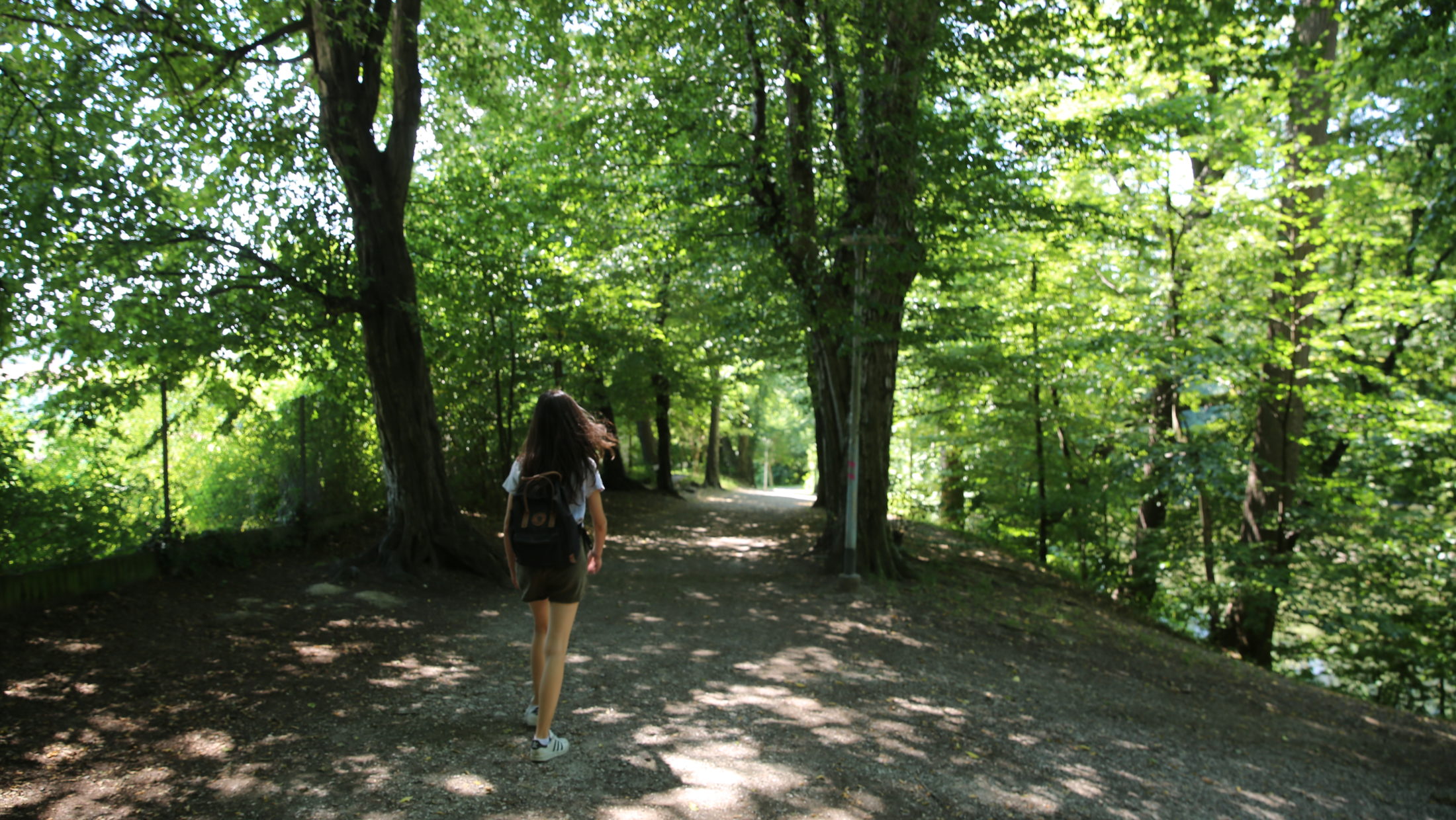 A young woman with a backpack walks along a wooded path at Rosenhain.
