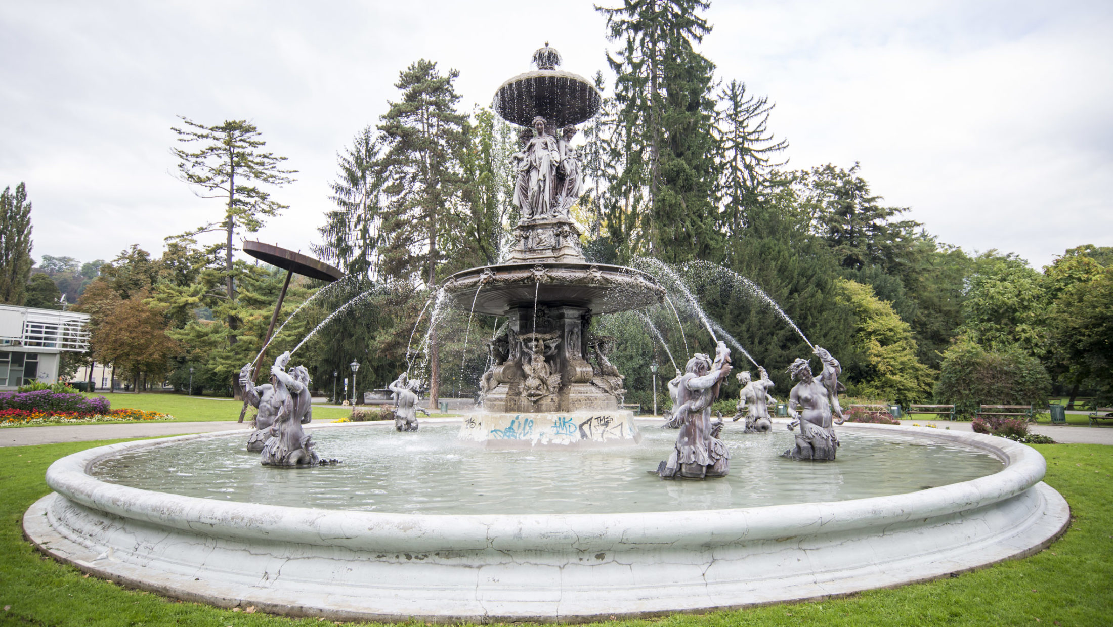 Das Bild zeigt den Stadtparkbrunnen, der mit Figuren verziert ist. Aus Fontänen spritzt Wasser.