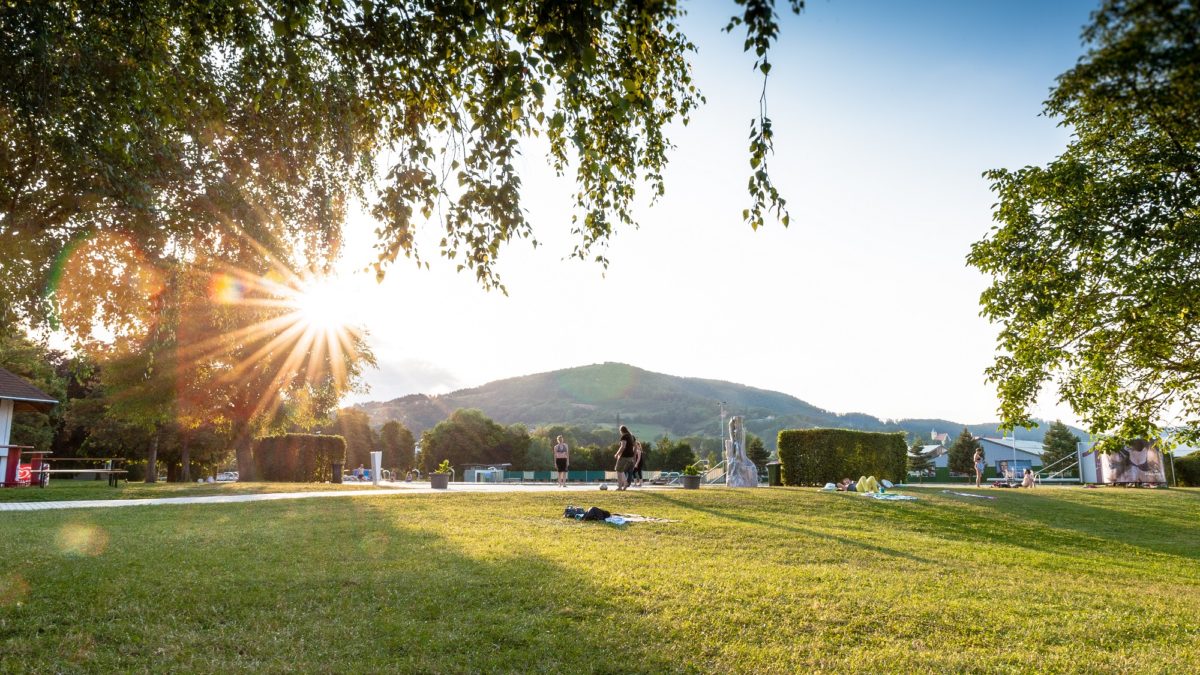 A grassy lawn with a few people at Bad Straßgang as the sun sets behind the hills.