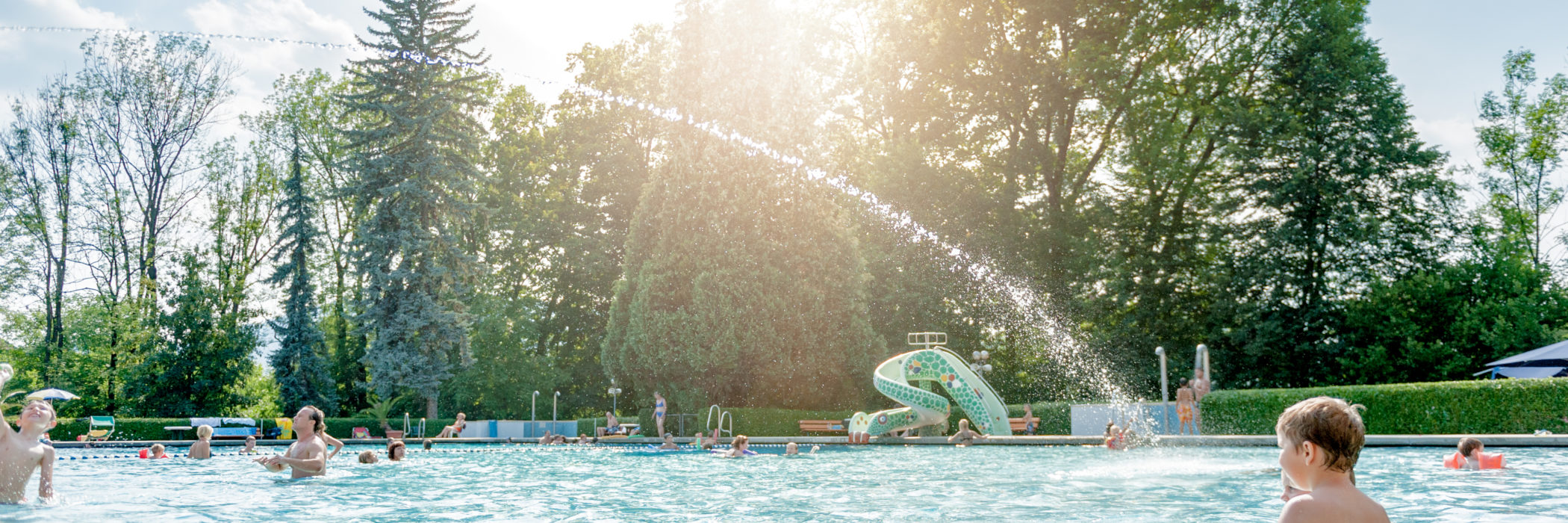 Gäste spielen im Becken des Stukitzbades, bunte Rutsche und Wassersprühstrahl sind zu sehen.