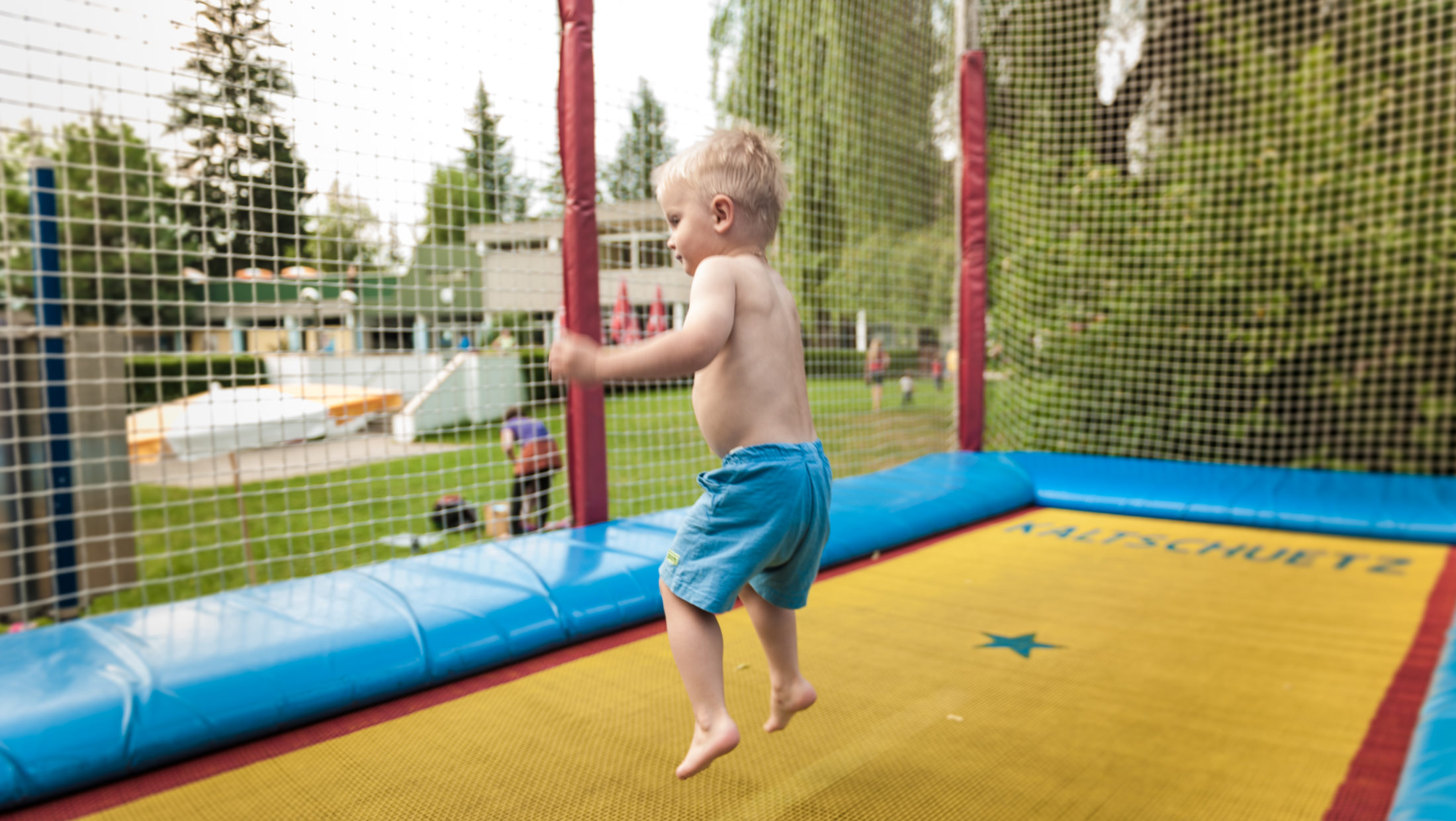 A young boy jumps on a trampoline labeled "Saltschuetz 12".