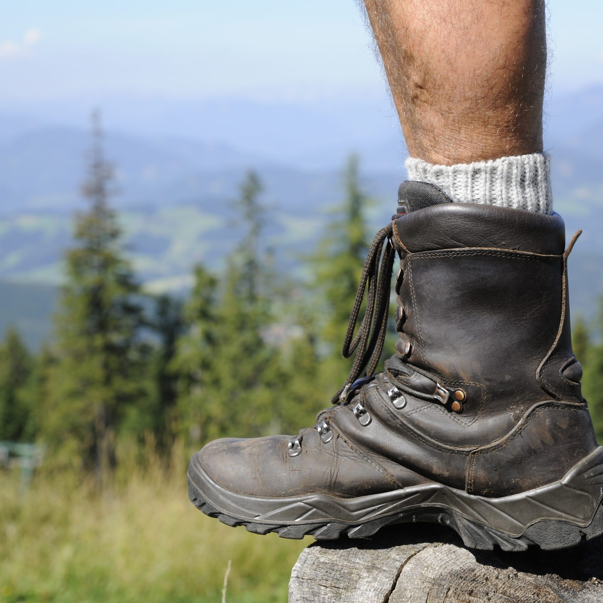 Männer-Bein mit Wanderschuh steht auf Holzbank am Schöckl. Im Hintergrund das Grazer Hügelland.