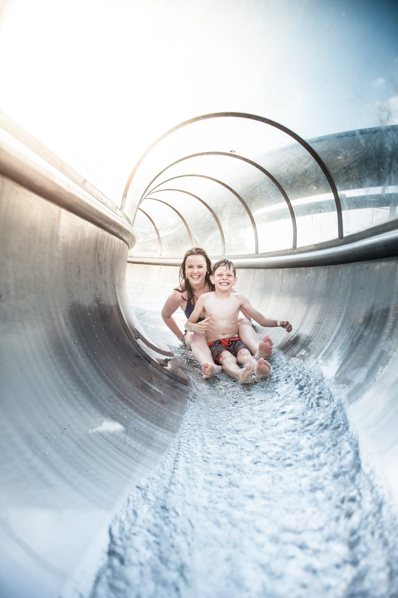 A woman and a young boy smile as they slide down a water slide.