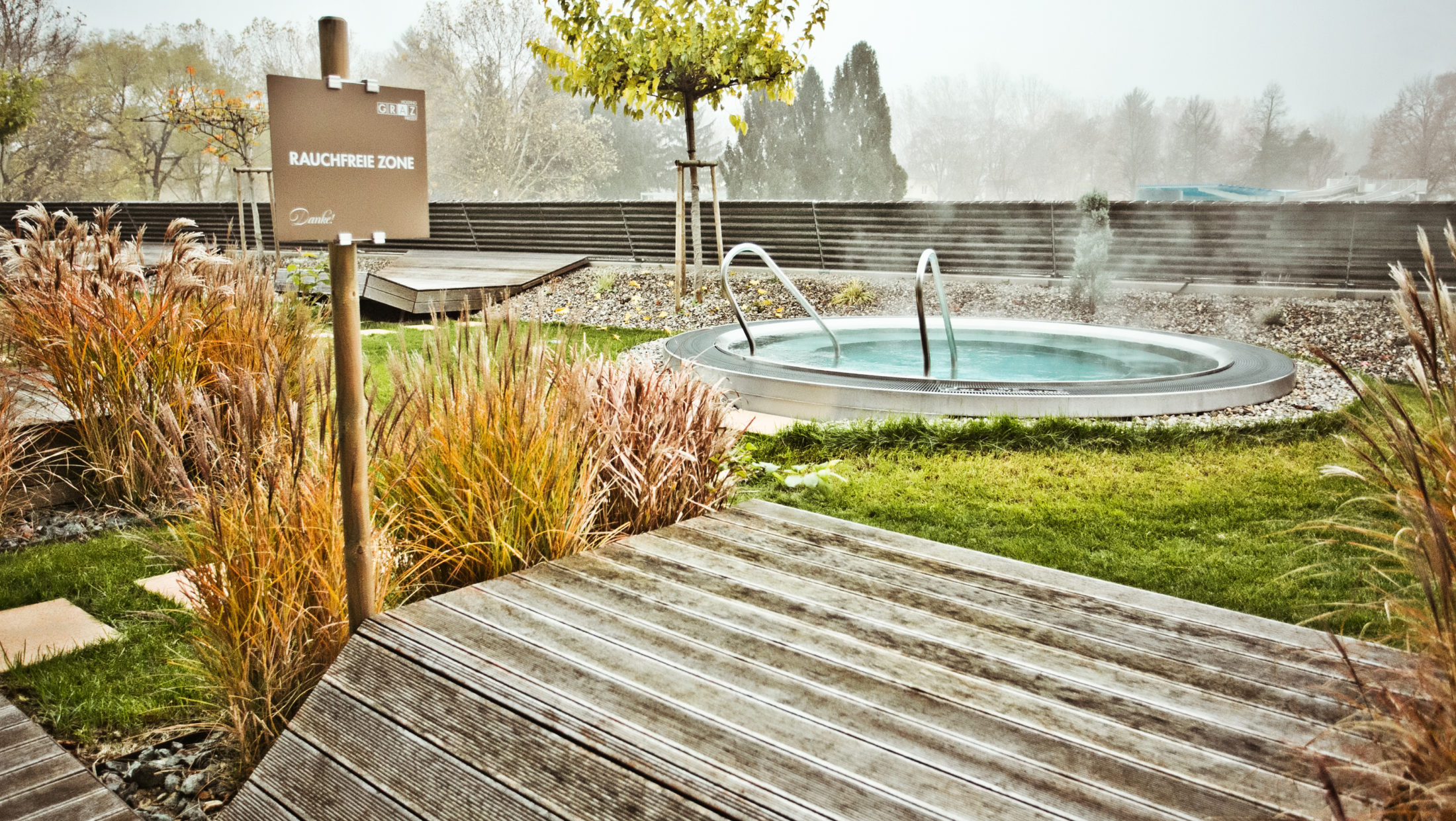 A wooden deck with a sign that reads "Rauchfreie Zone" (Non-Smoking Zone) and a hot tub in the background.