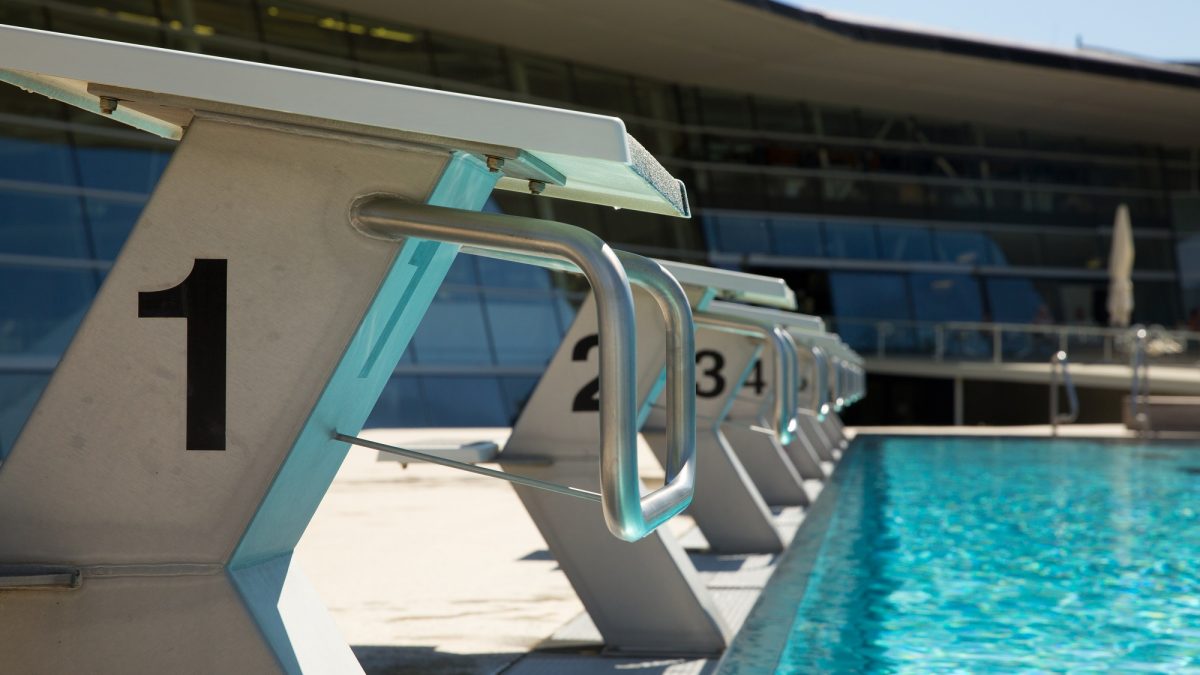 A row of numbered diving blocks next to a swimming pool.