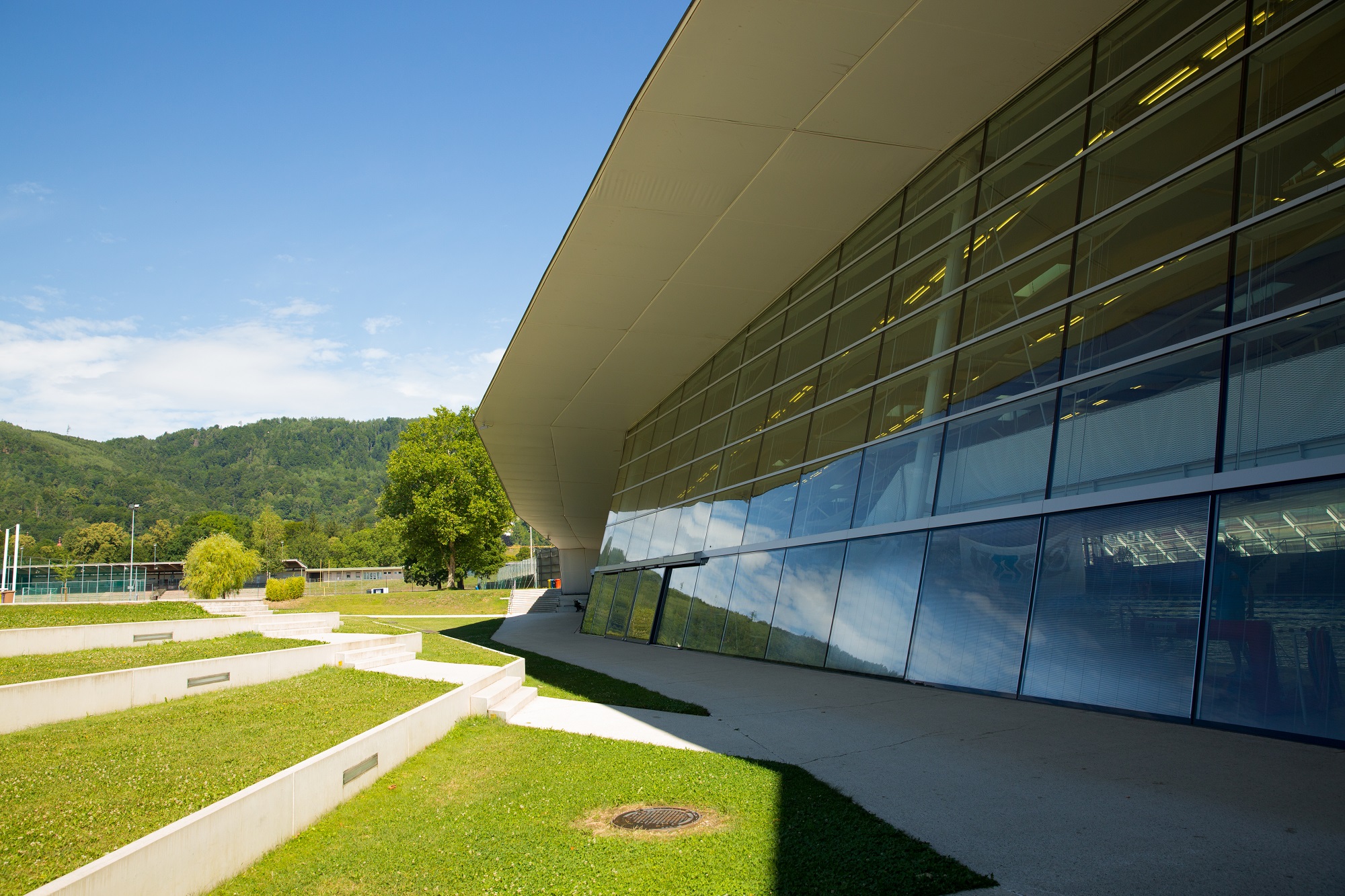 The Auster's outdoor area with a grassy lawn, terraced seating, and a glass facade revealing an indoor pool.