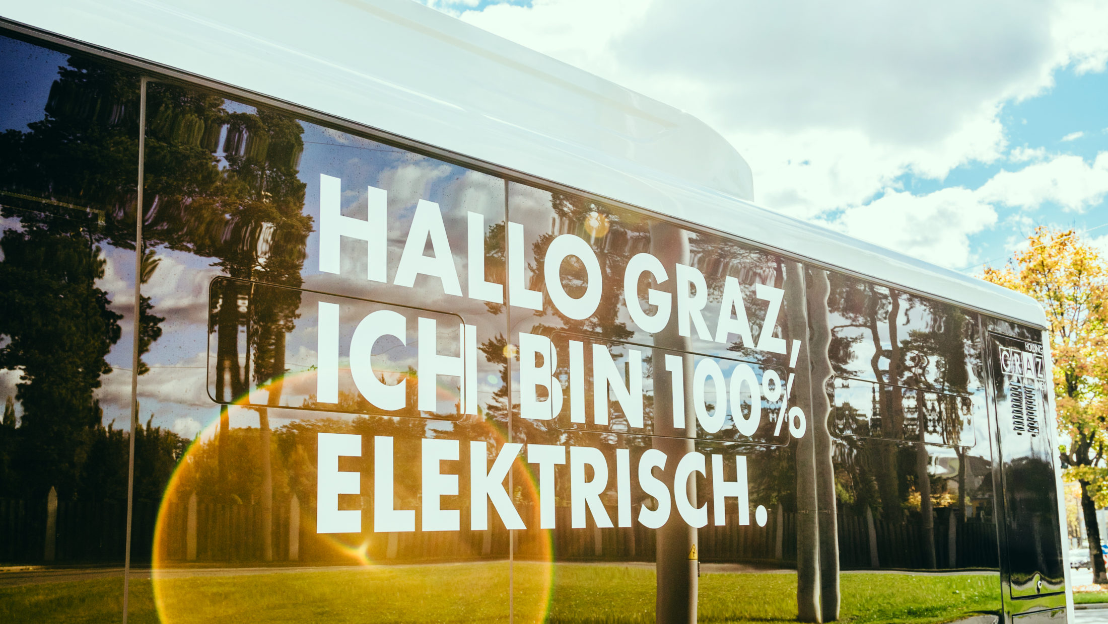 A white electric bus in Graz, Austria, with the message "Hallo Graz, Ich bin 100% Elektrisch." on its side.