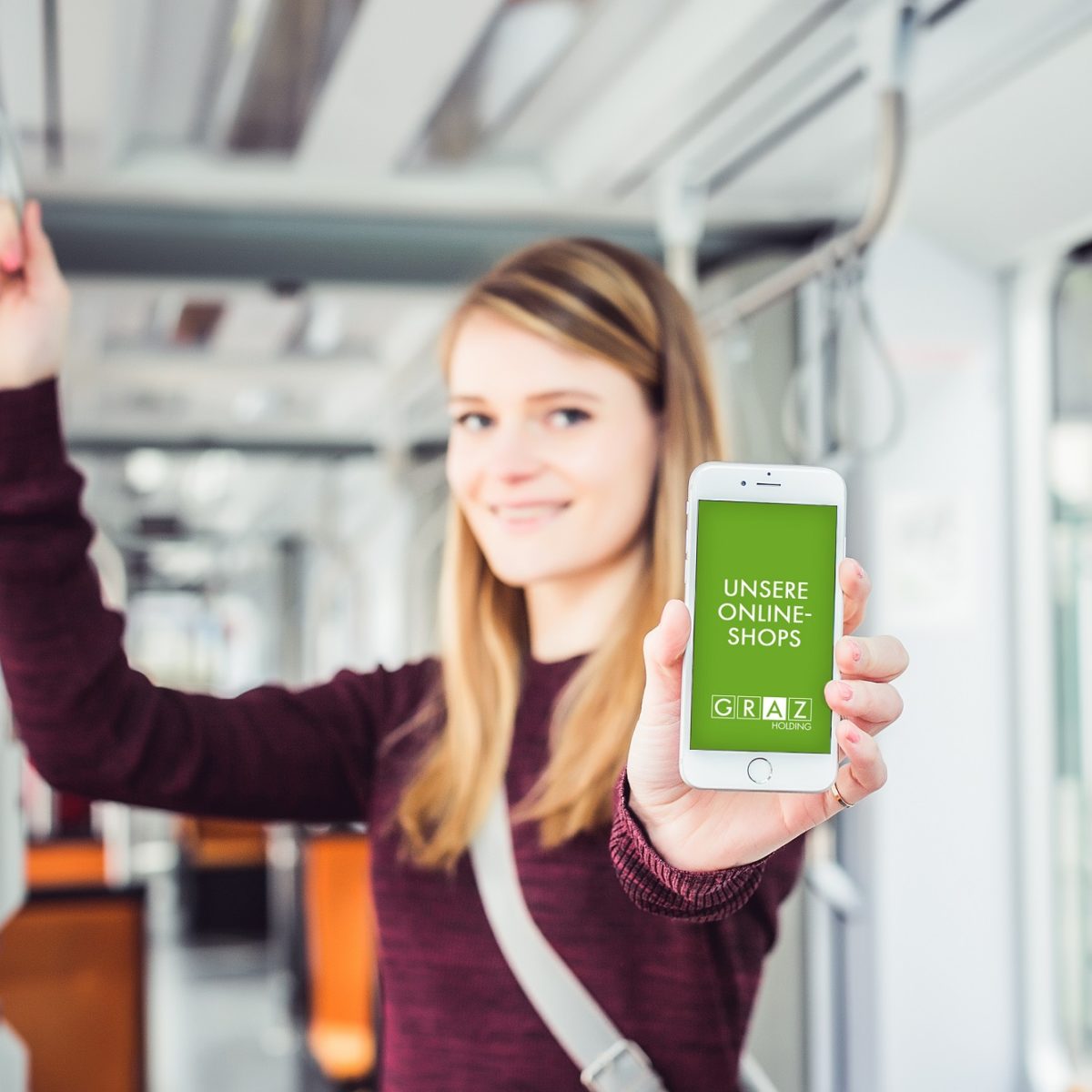 Young woman stands in tram and shows mobile phone with open GrazMobil app into picture