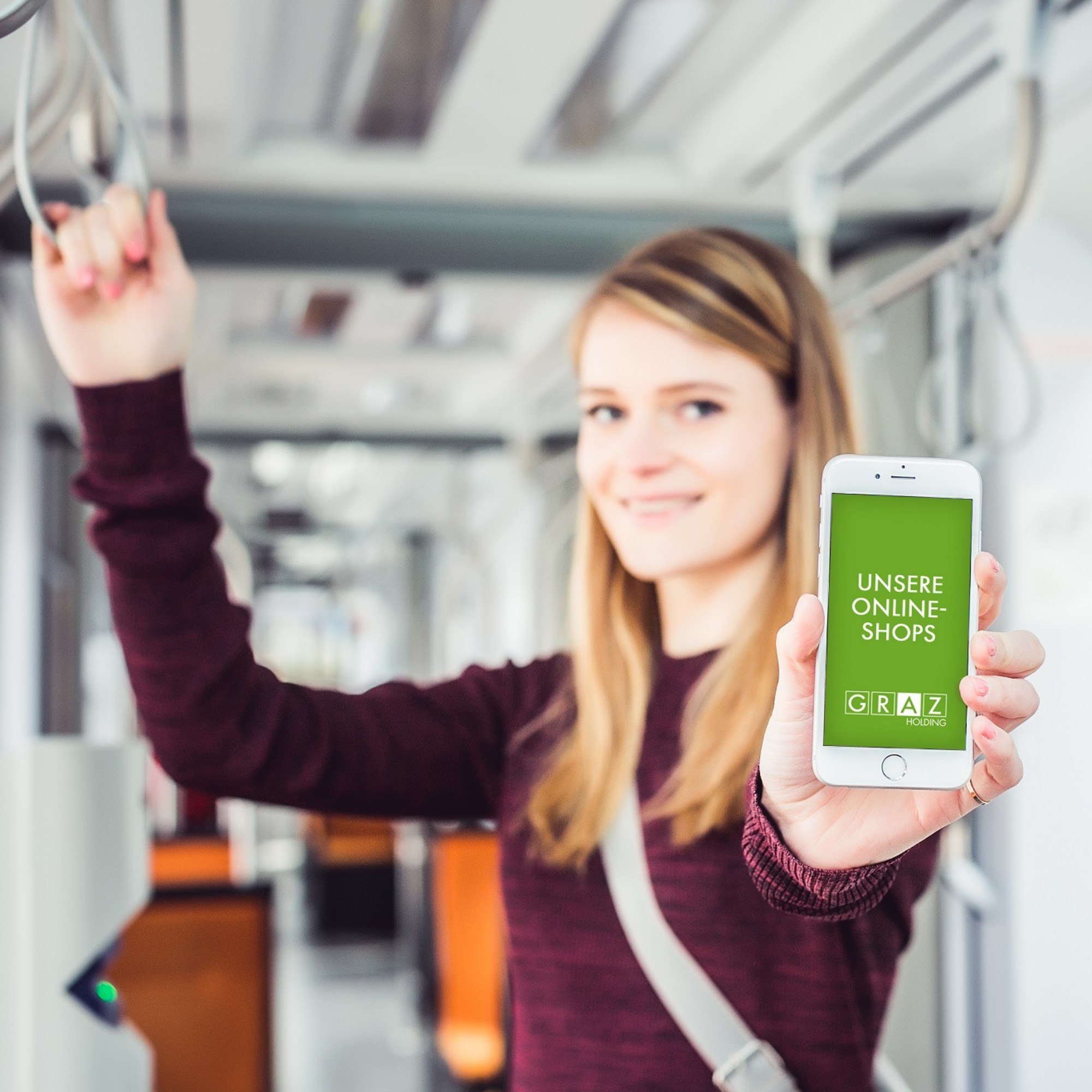 Junge Frau in der Straßenbahn zeigt ein Smartphone mit der "GrazMobil"-App auf dem Bildschirm.