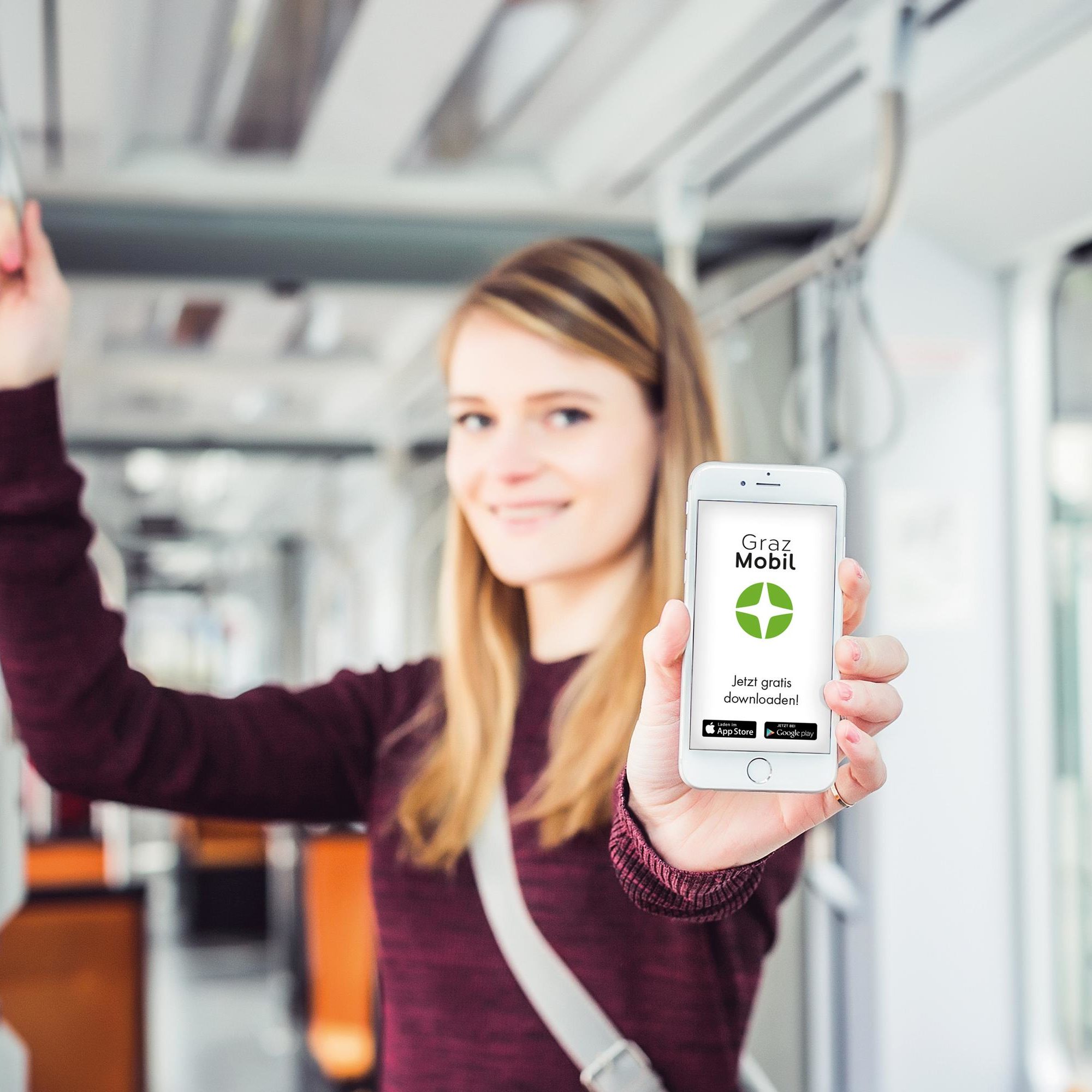Junge Frau in der Straßenbahn zeigt ein Smartphone mit der "GrazMobil"-App auf dem Bildschirm