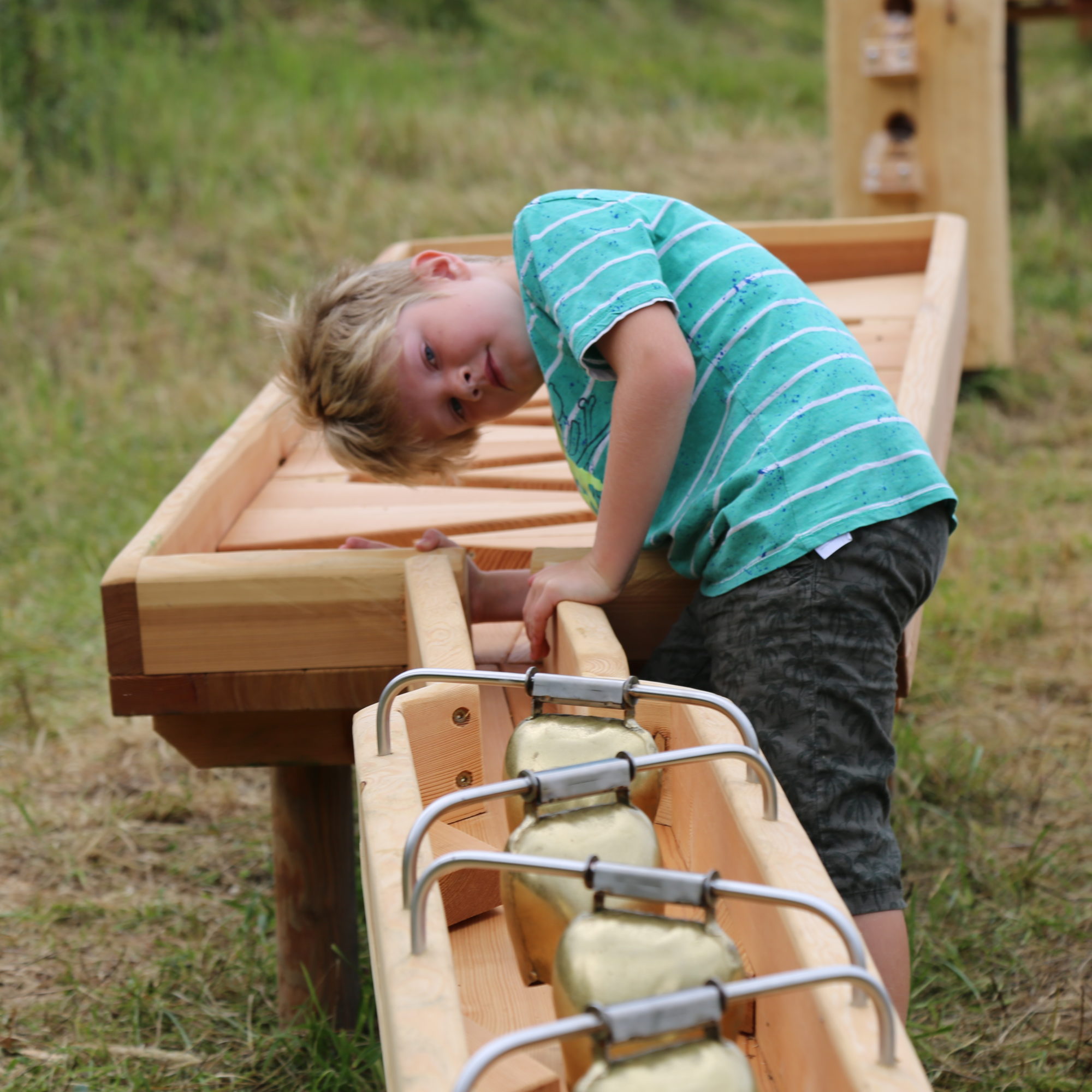 A young boy looks over the edge of a wooden structure with bells attached to a track.