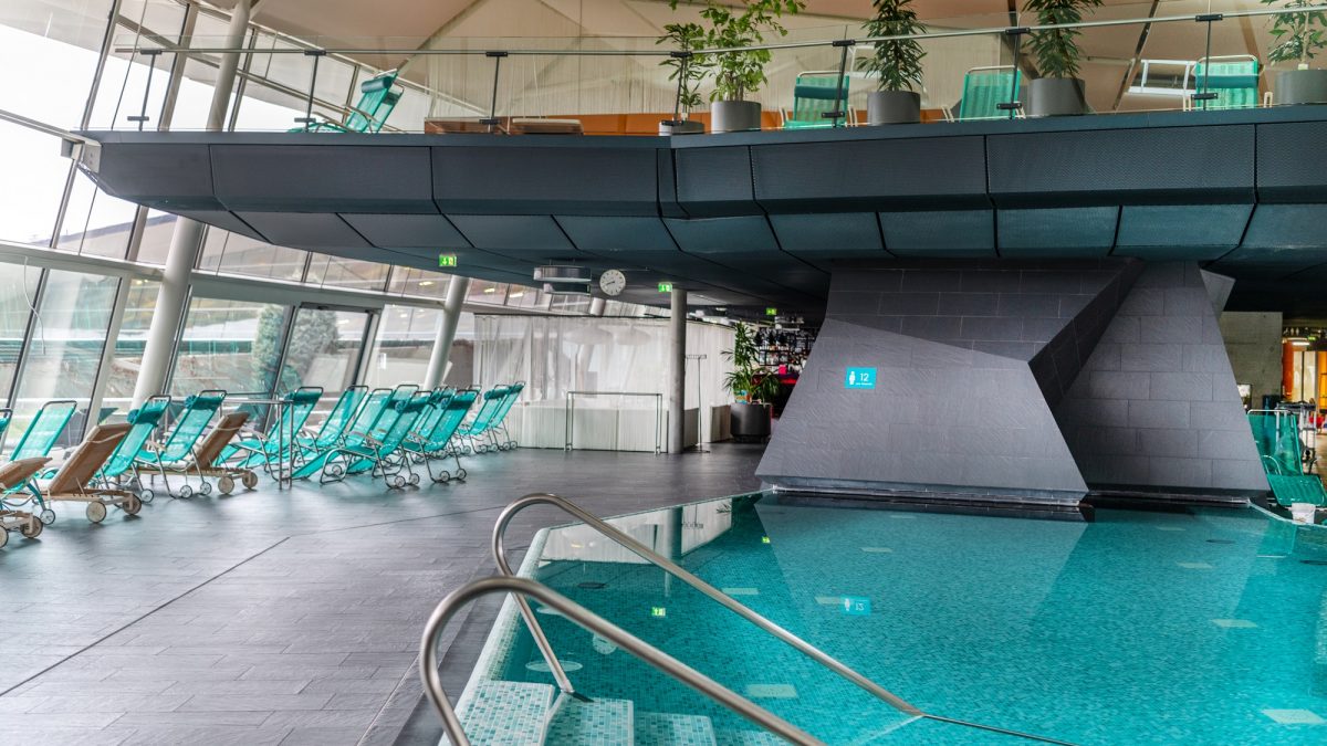 Indoor pool with teal lounge chairs and a raised platform with more chairs, a sign indicating "WC" is visible.