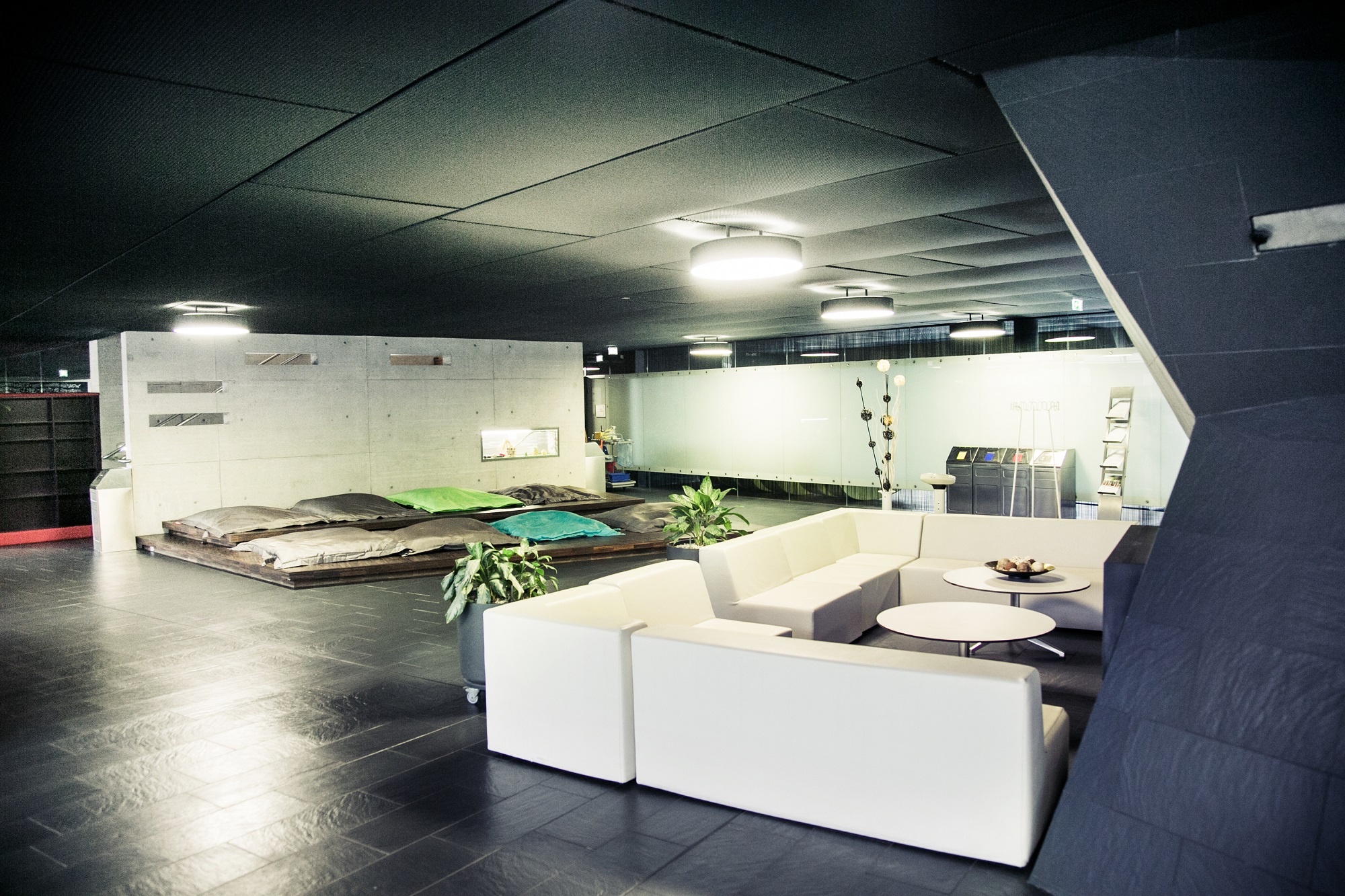 A modern waiting area with white couches, a platform with cushions, and plants in the Auster wellness area.