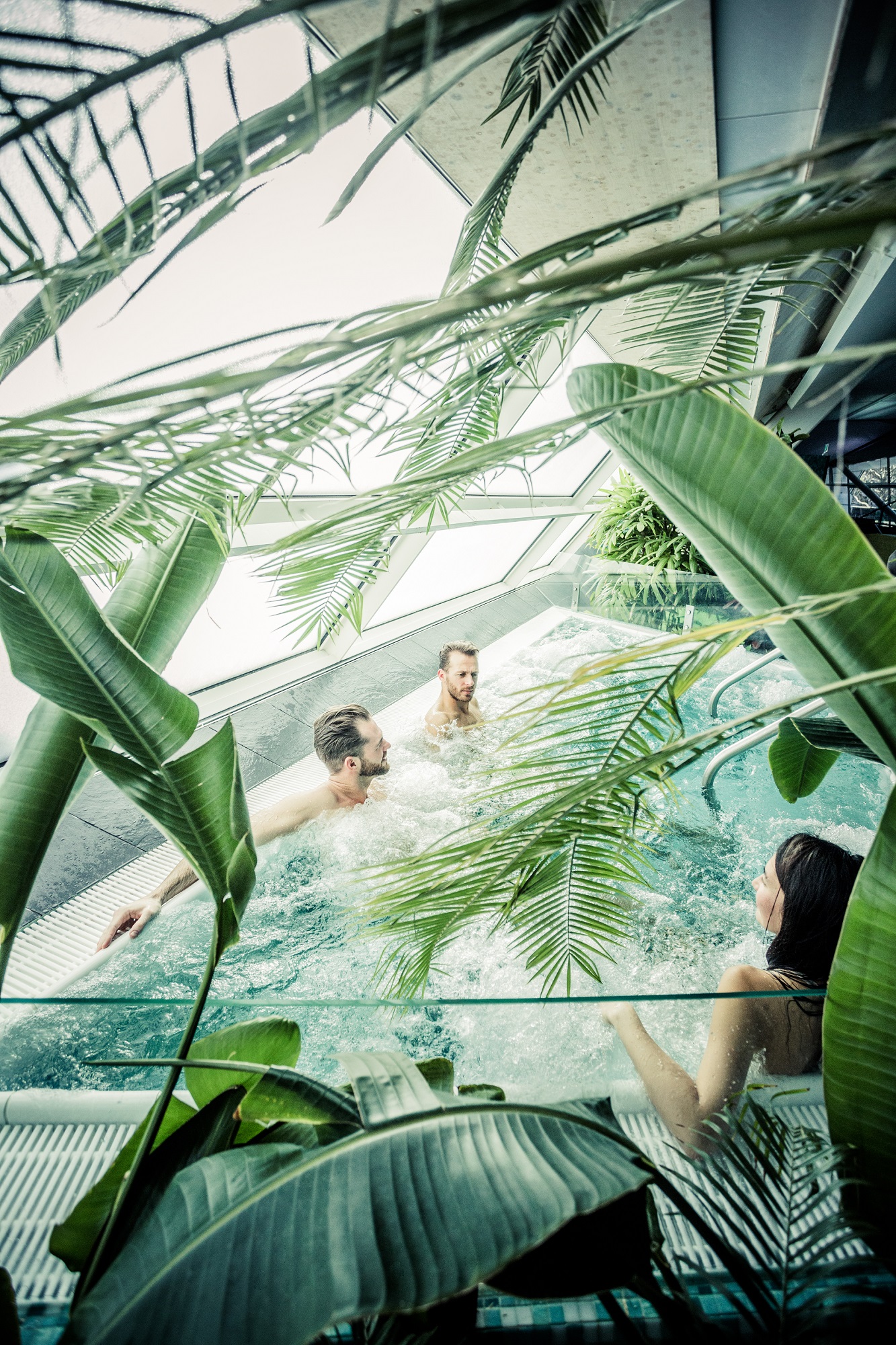 Three people relax in a hot tub surrounded by tropical plants at the Auster wellness area.