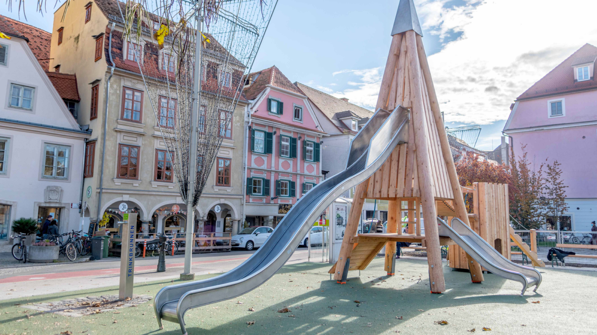 Spielplatz Kapistran-Pieller-Platz mit Klettergerüst aus Holz in Form eines Turms mit zwei Rutschen.