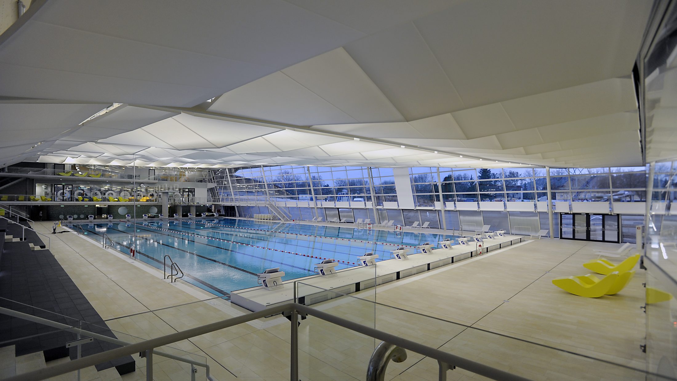 A view of the Auster Sports Pool, featuring a large indoor swimming pool, with yellow chairs in the foreground.