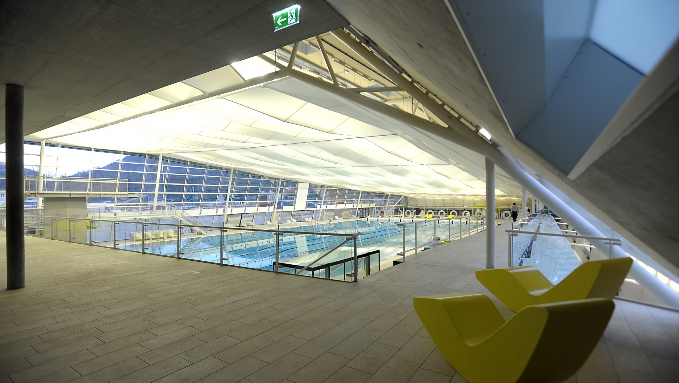 Auster Sportbad: Innenansicht mit Schwimmbahnen, gelben Liegestühlen und Glasfront.