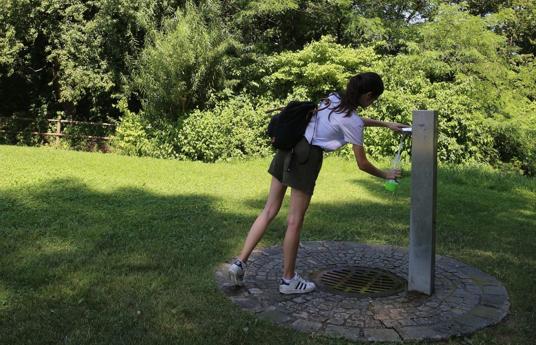 Lustbühel: Das Bild zeigt Frau, die mit Flasche Wasser aus Trinkbrunnen auffüllt.