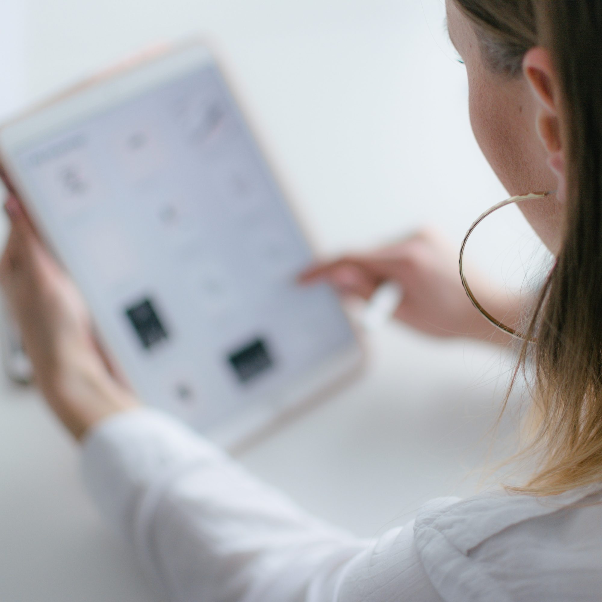 Eine Frau mit großem Ohrring tippt vor weißem Hintergrund Daten in ein Tablet ein