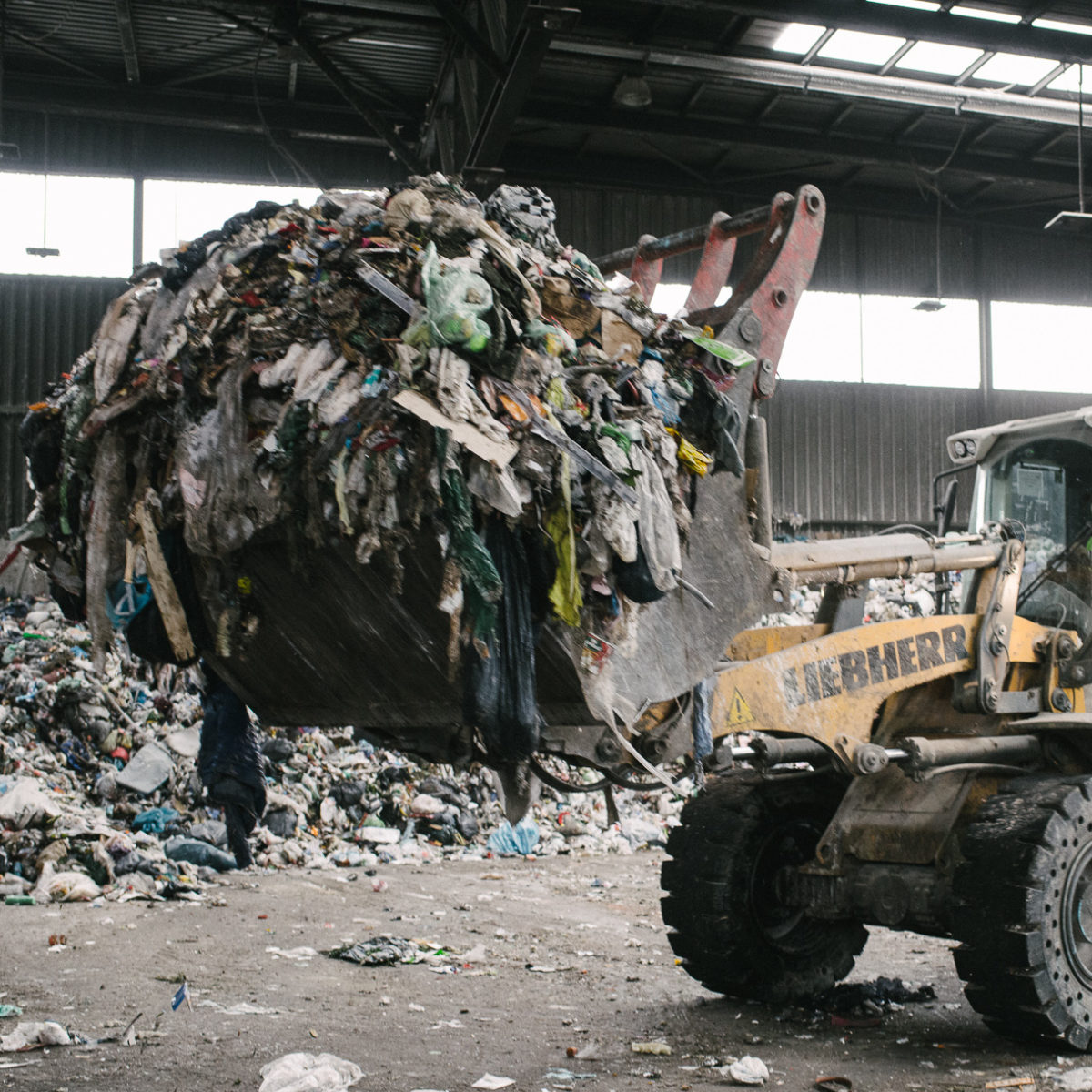 A Liebherr loader lifts a large pile of garbage at a waste processing facility.