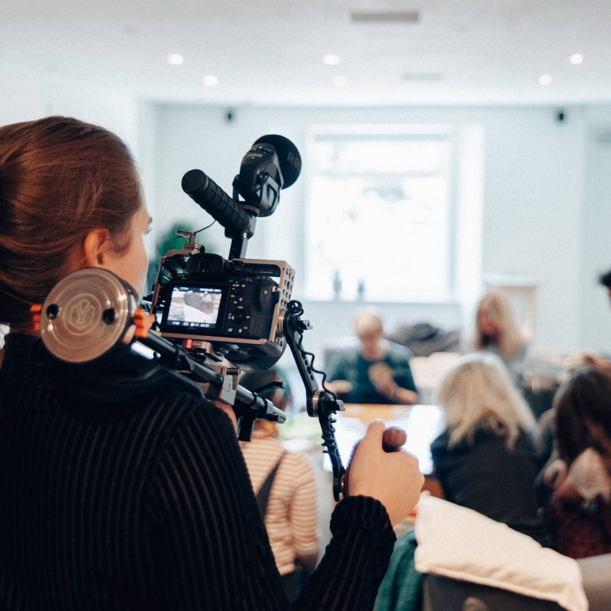 A woman films a group of people sitting at a table.