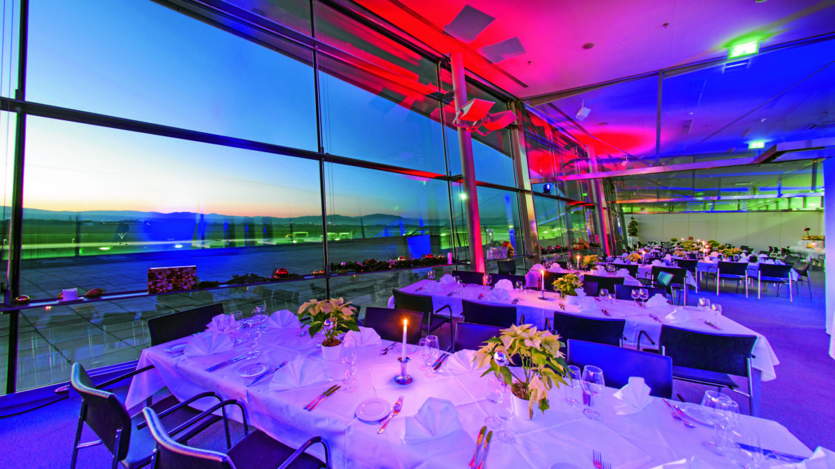 An empty restaurant at Graz Airport with festively set tables and a view of the runway.