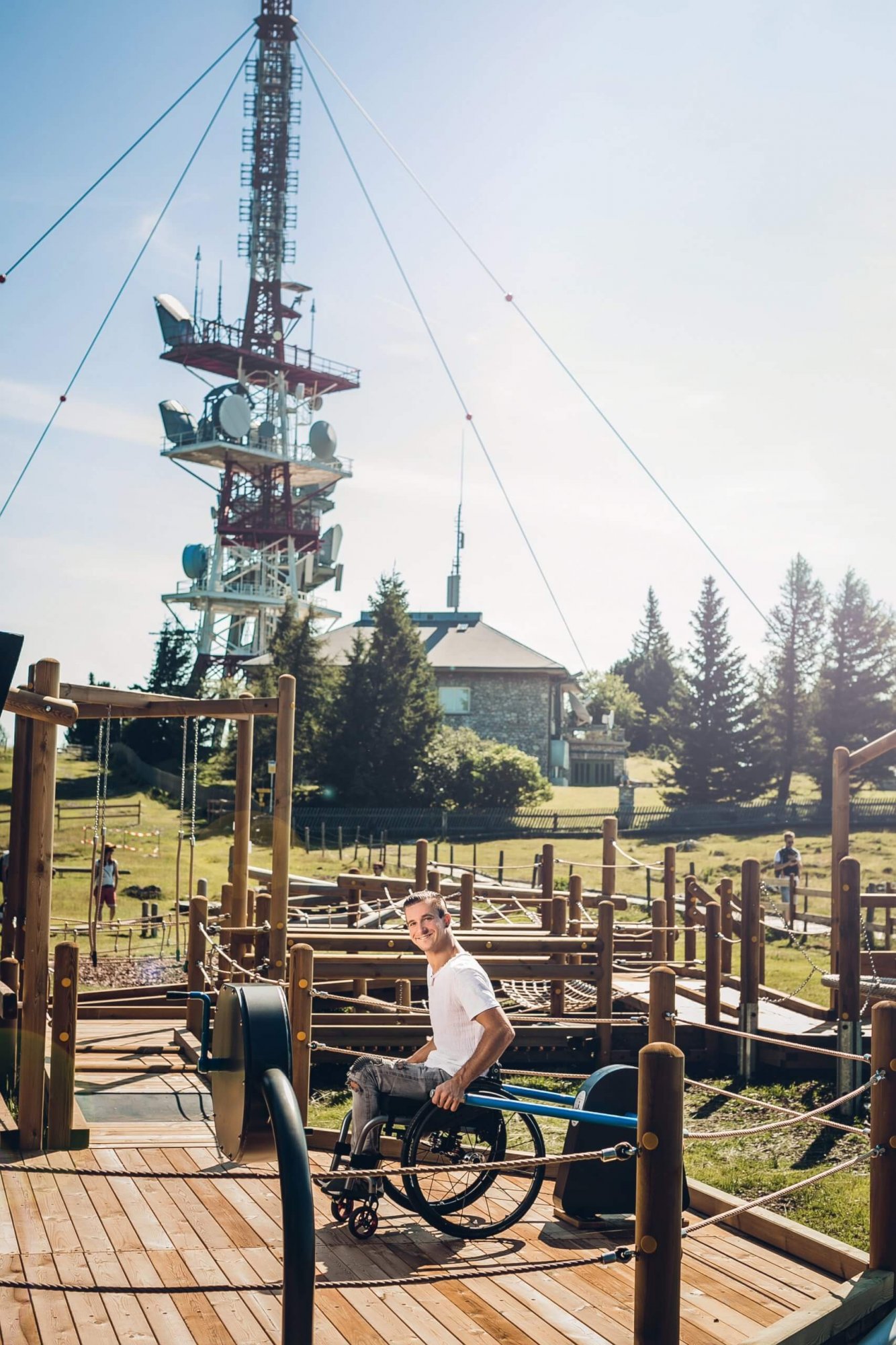 Rollstuhlfahrer steht auf Holzplateau des Motorikparkour am Schöckl. Im Hintergrund sieht man Sendeanlage.
