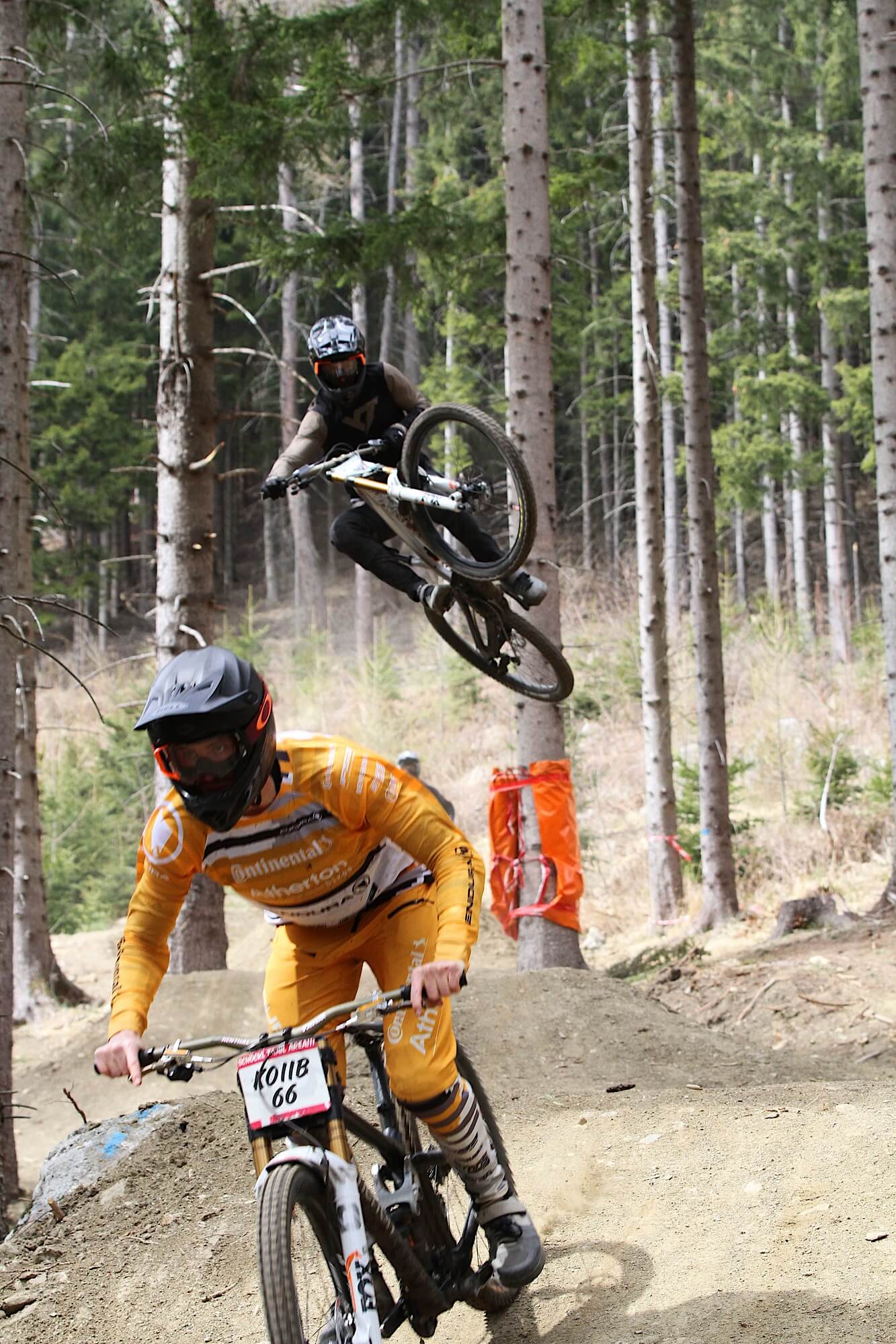 Two mountain bikers ride down Schöckl Trail Area one behind the other, the rider in the back just makes a high jump with the bike.