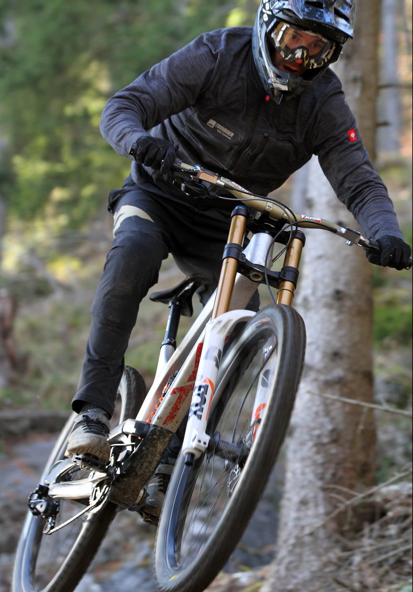 Mountainbiker mit Helm und Schutzkleidung fährt mit hoher Geschwindigkeit durch einen Wald.