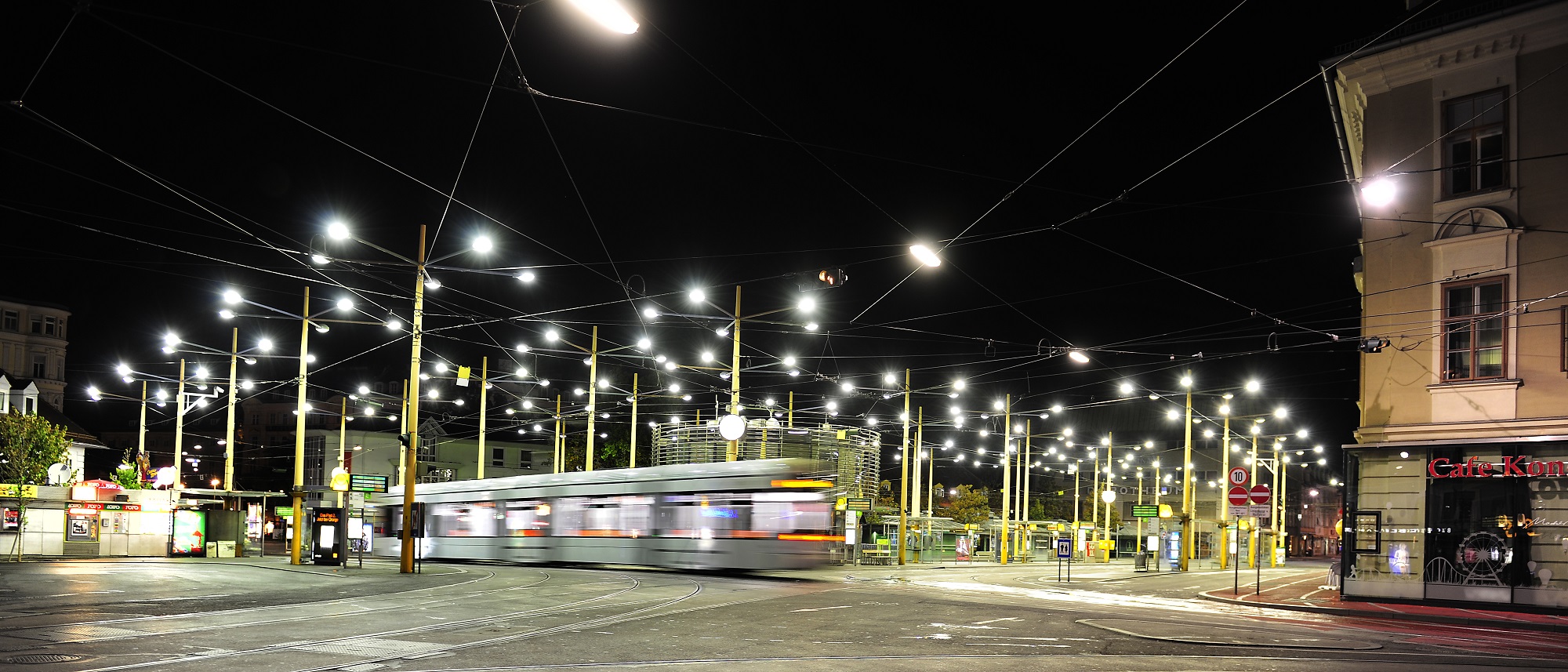 A tram passes through Jakominiplatz at night, illuminated by streetlights.