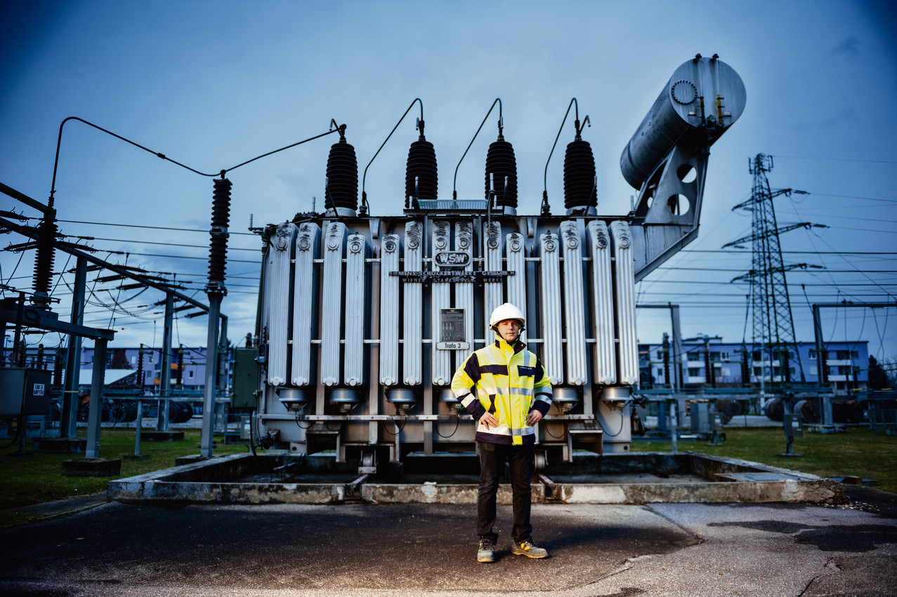 Arbeiter in Schutzkleidung und mit Schutzhelm steht vor Transformator in Umspannwerk.