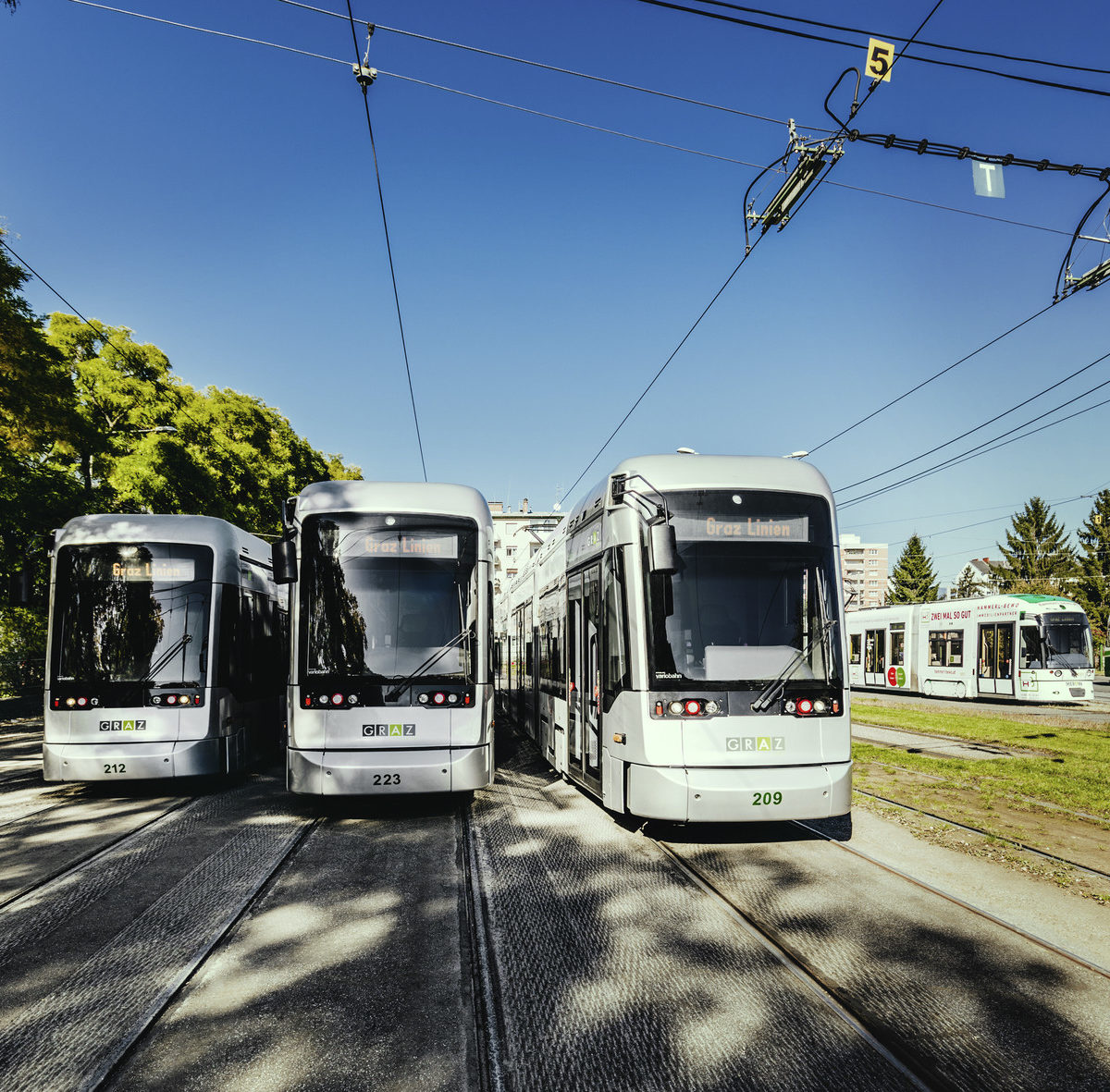 Three Variobahn tram sets on tracks in the open-air area of the Remise. Older tram models to the side behind them
