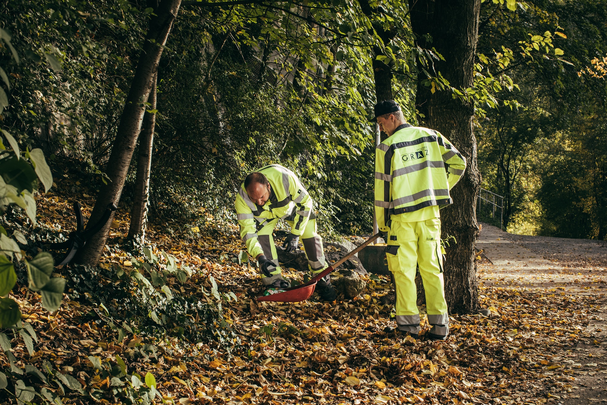 Mitarbeiter des Stadtraumes in Arbeitsuniform sammeln Laub am Murufer ein