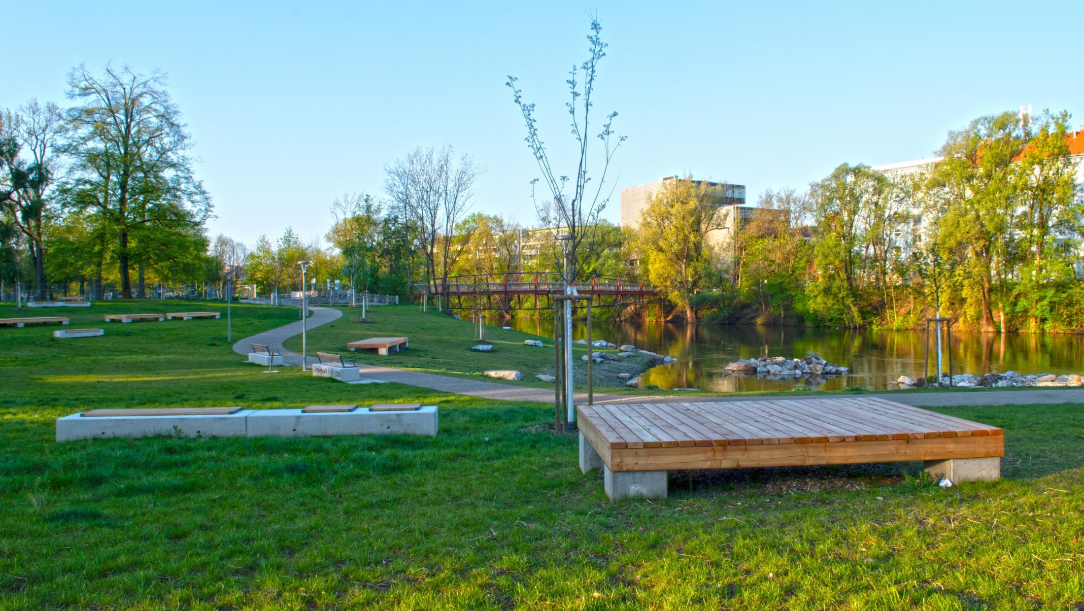 Empty benches in a grassy park with a river and bridge in the background.