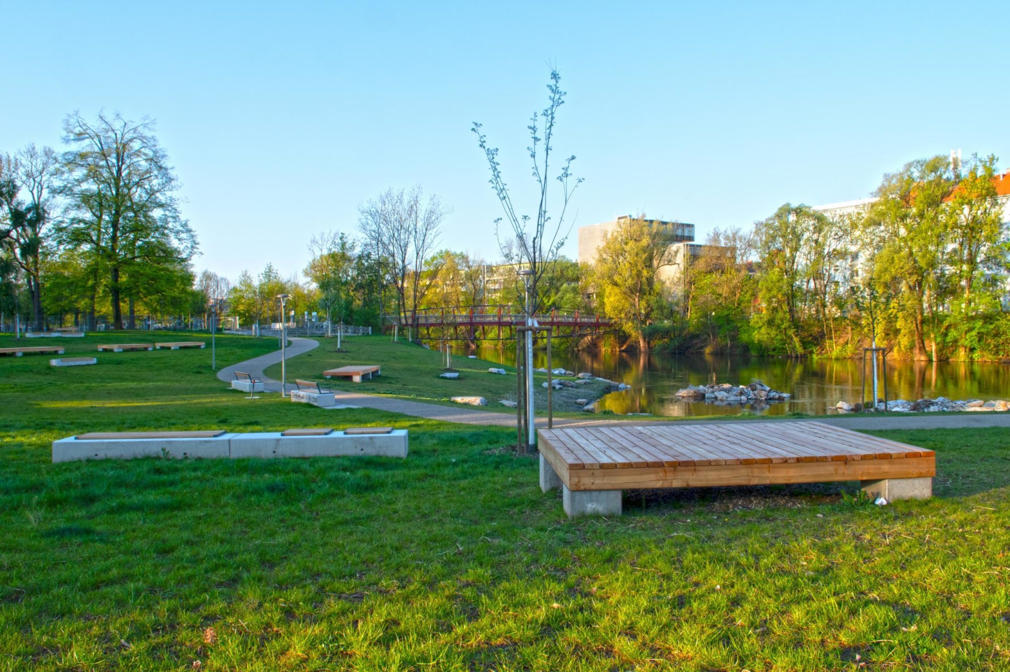 Empty benches in a grassy park with a river and bridge in the background.