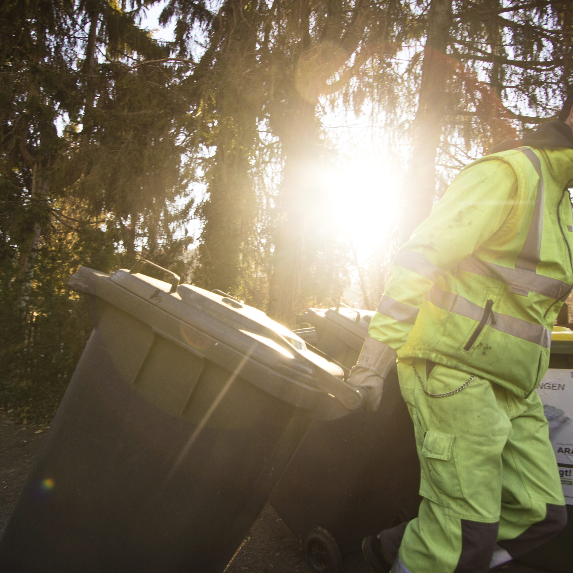 Mitarbeiter der Holding Graz in Arbeitskleidung zieht großen Müllbehälter entlang eines Weges.