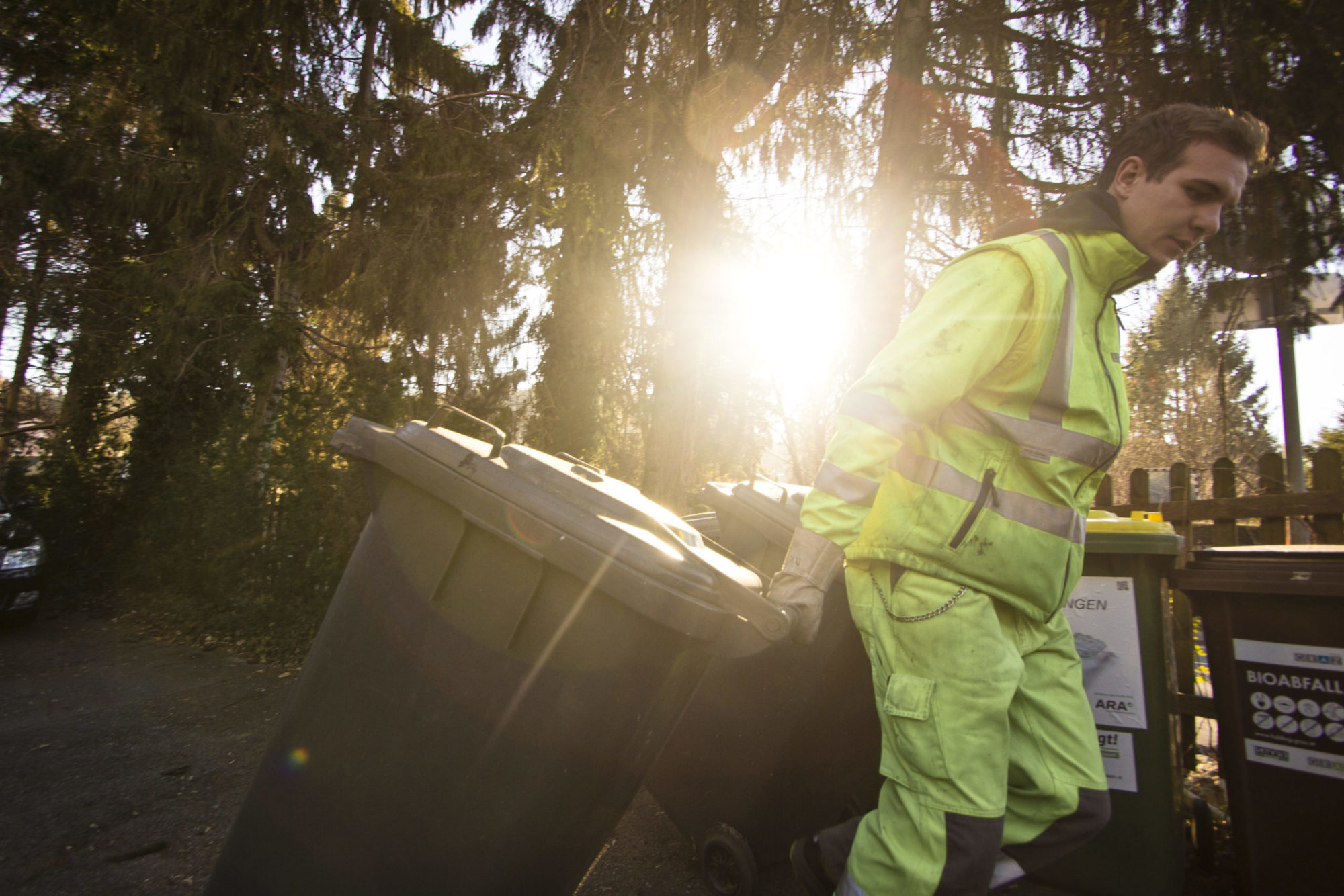 Mitarbeiter der Holding Graz in Arbeitskleidung zieht großen Müllbehälter entlang eines Weges.