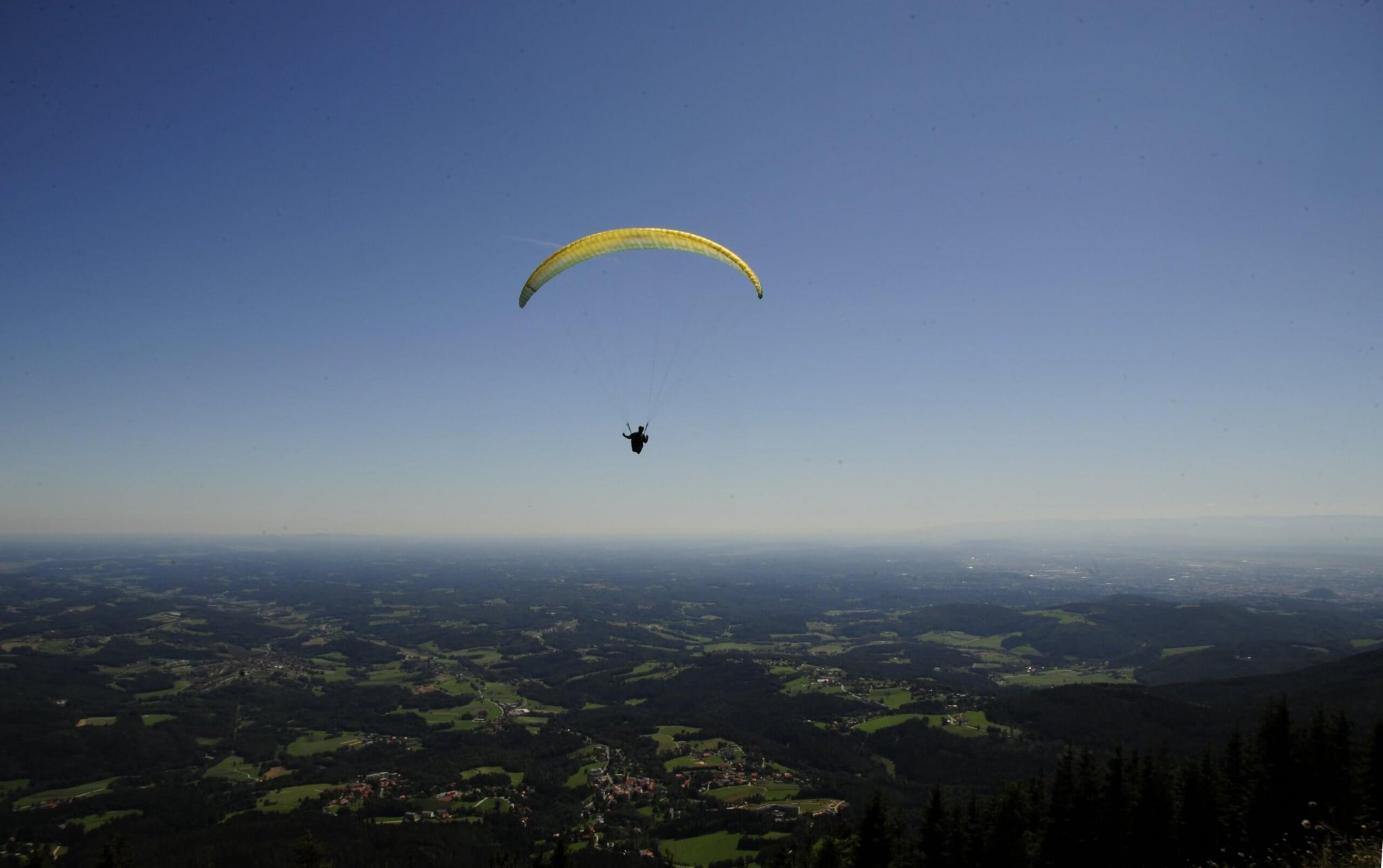 Paragleiter mit gelbem Schirm fliegt über das Hügelland nahe des Schöckls