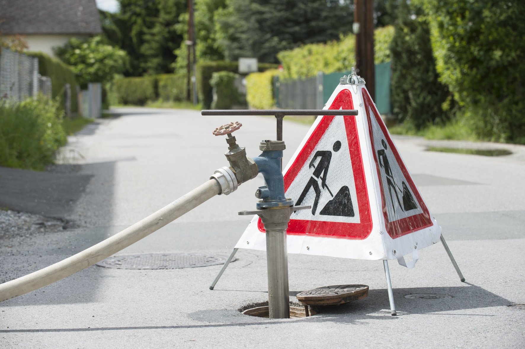 Verkehrszeichen "Achtung, Baustelle!" steht vor offenem Kanalschacht, in den Wasserleitung führt