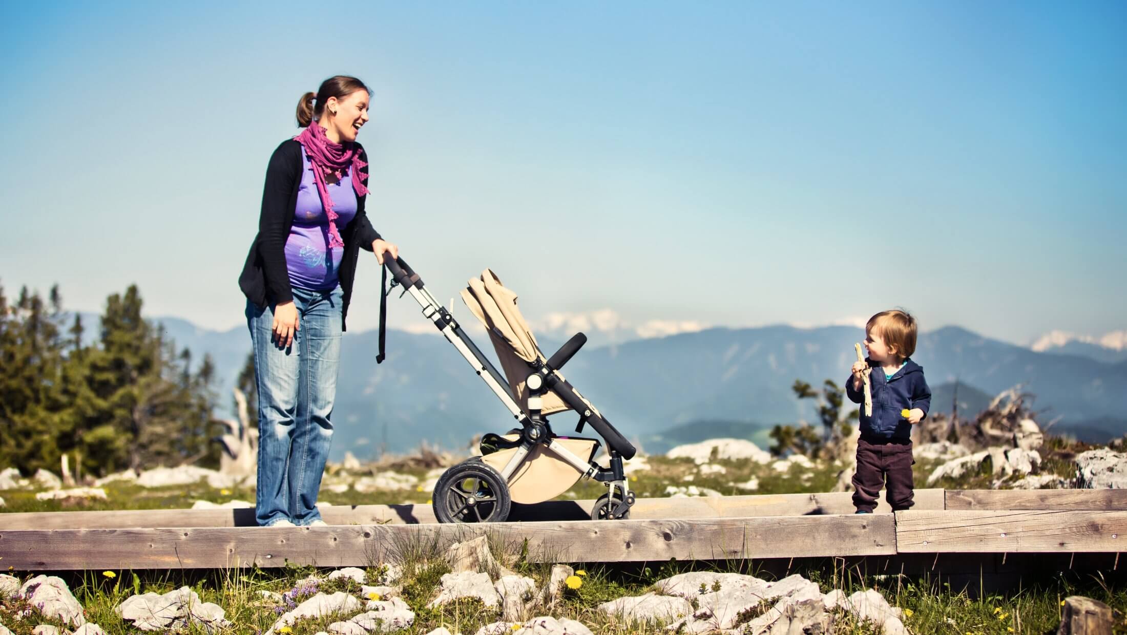 Mutter mit Kleinkind und Kinderwagen stehen am barrierefreien Holzweg am Schöcklplateau.